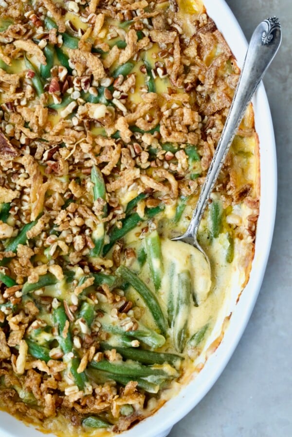 Cheesy Green Bean Casserole in white oval gratin dish with serving spoon.