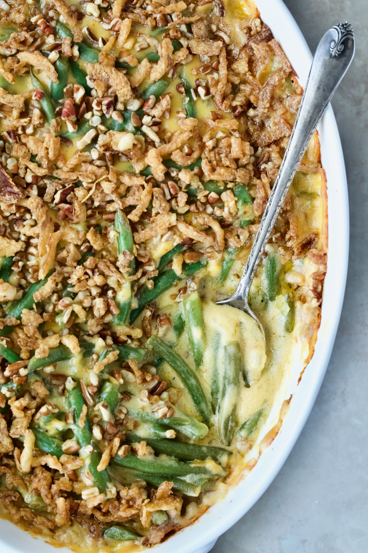Cheesy Green Bean Casserole in white oval gratin dish with serving spoon.