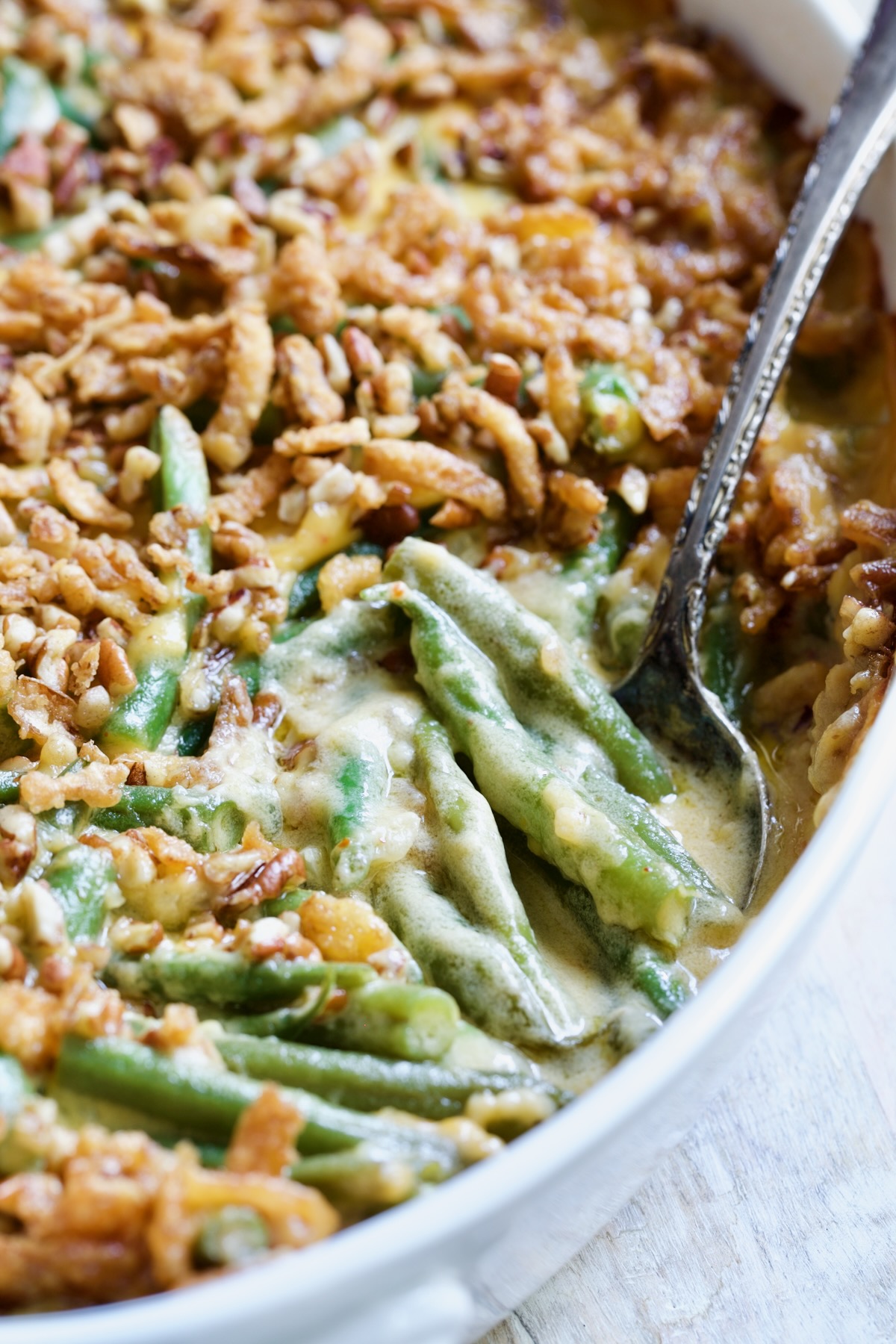 Cheesy Green Bean Casserole with pecan and crispy onion topping with serving spoon.