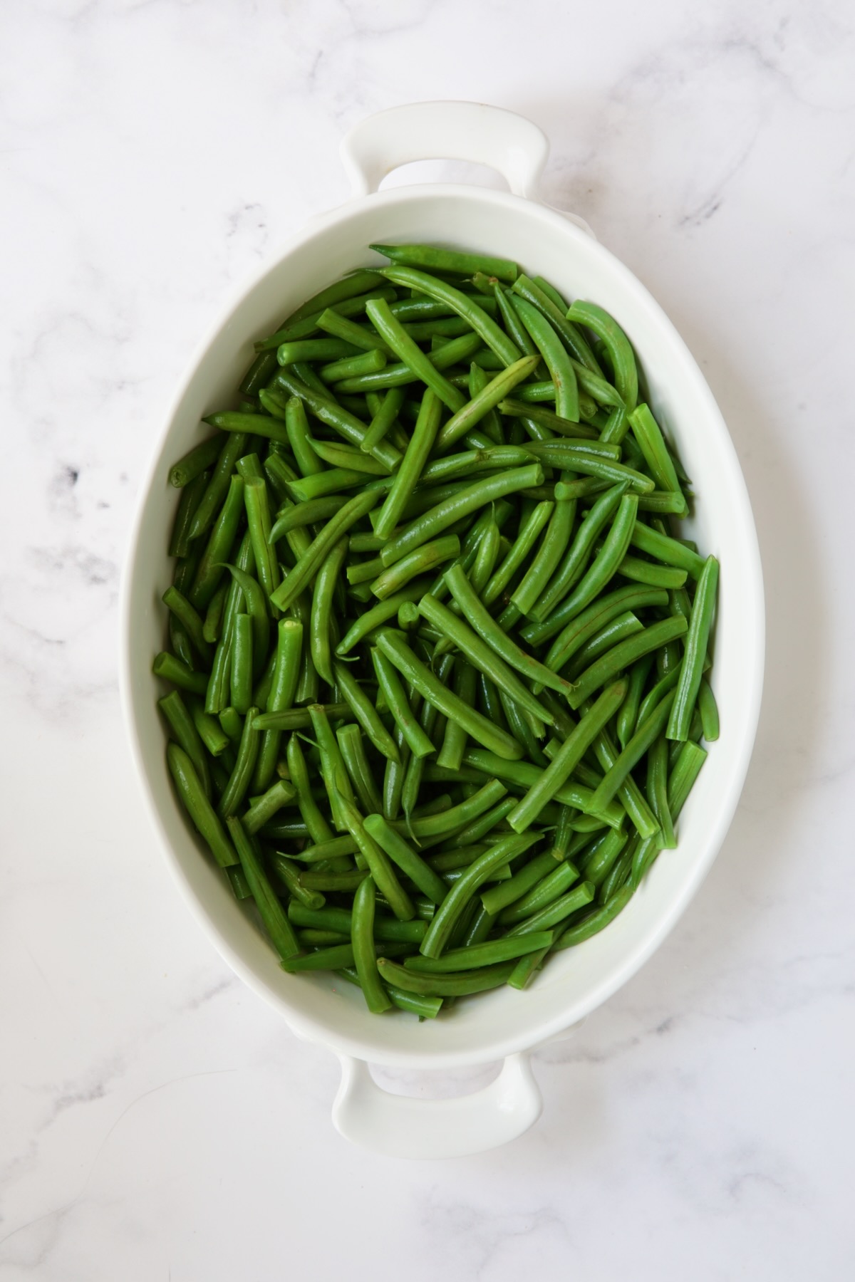 Blanched green beans in white oval gratin dish.