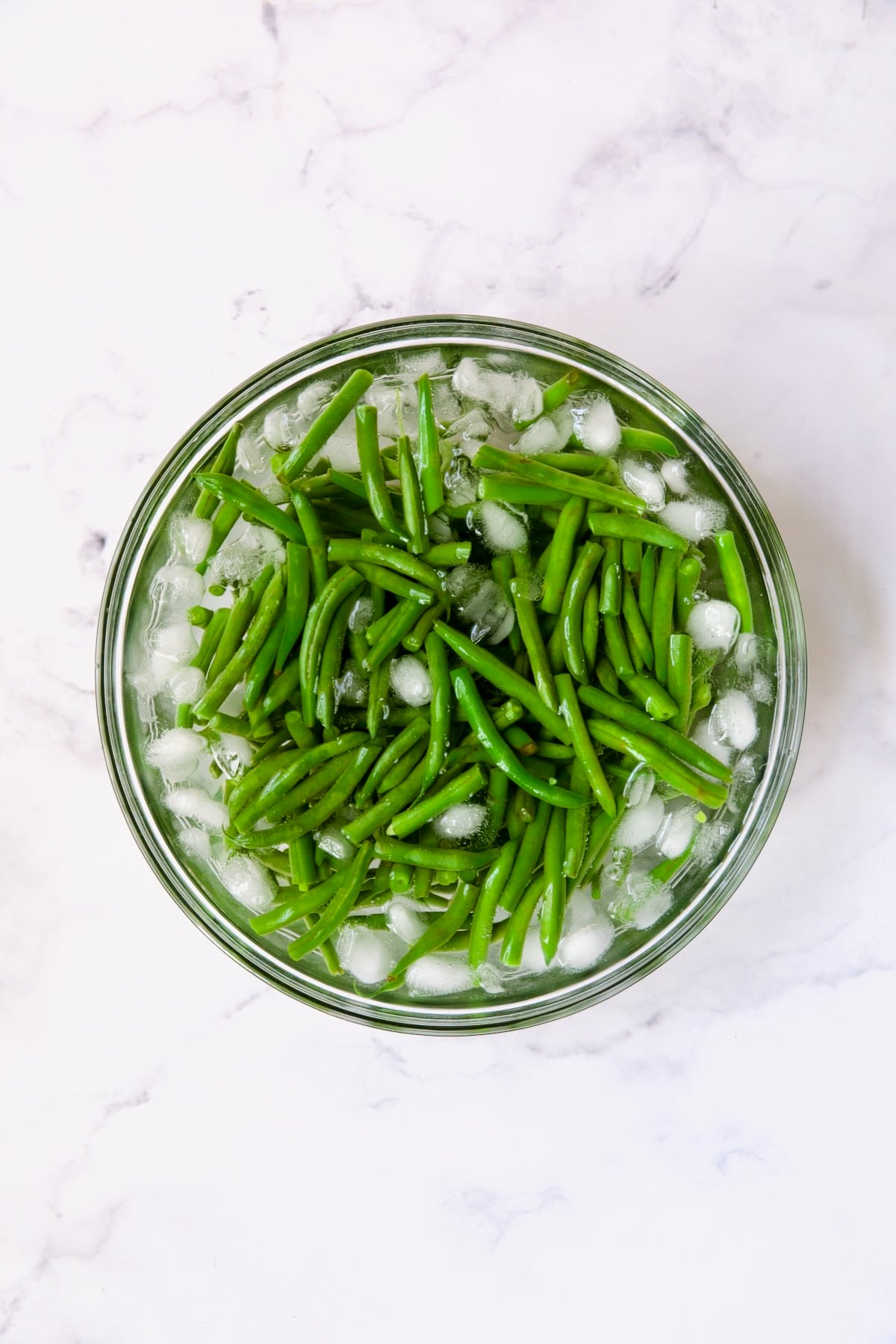 Green beans in ice water in glass bowl.
