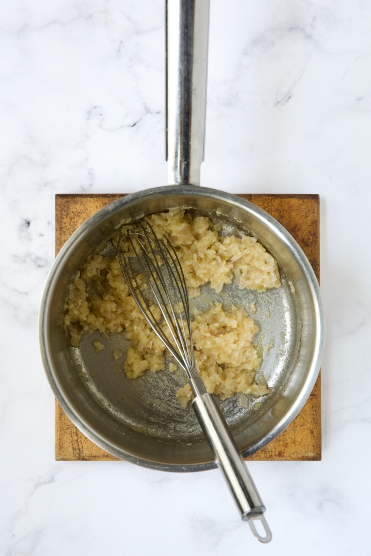 Shallot, garlic and flour with wire whisk in stainless steel saucepan.