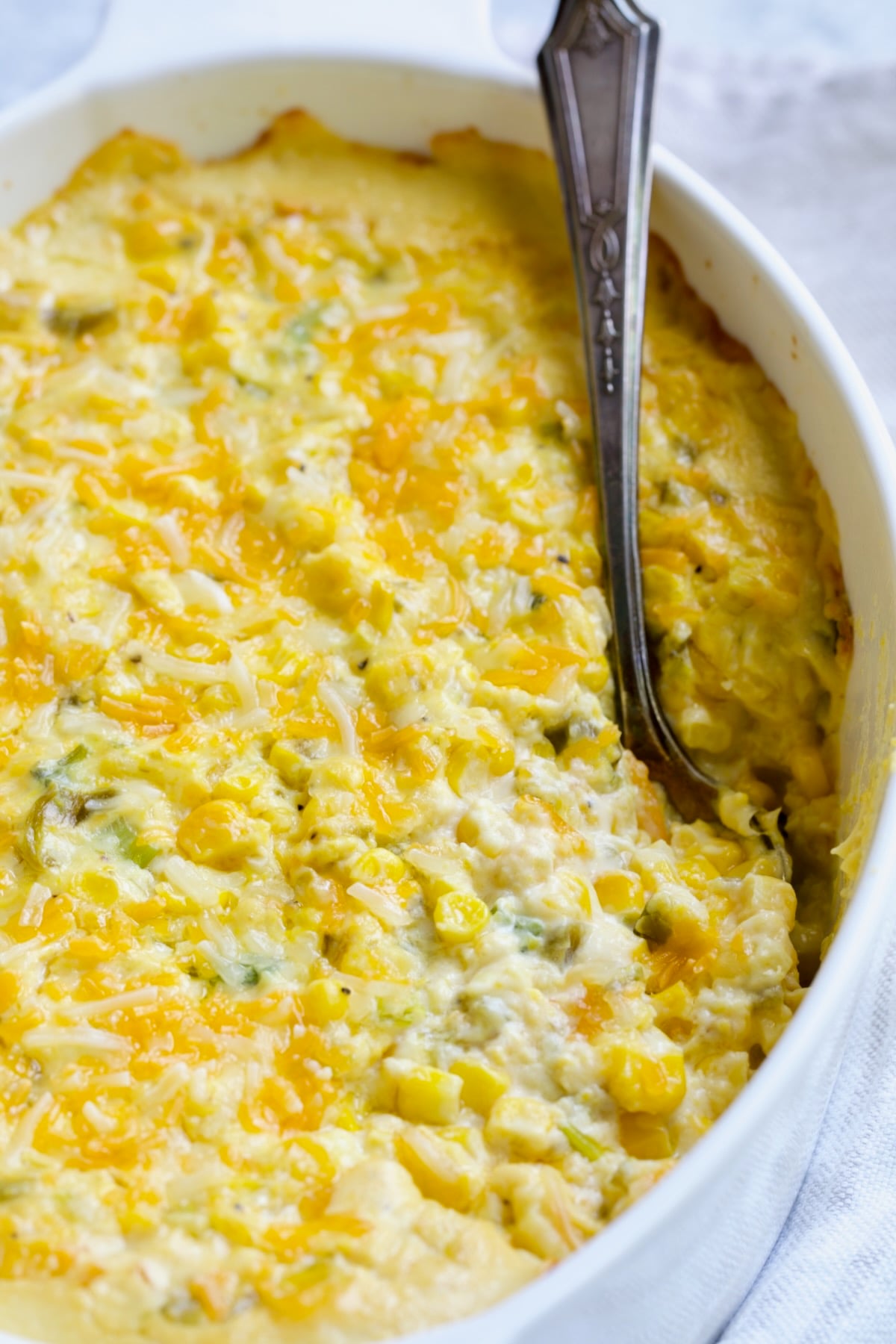 Cream Cheese Corn Casserole with Green Chiles in white oval baking dish with serving spoon.