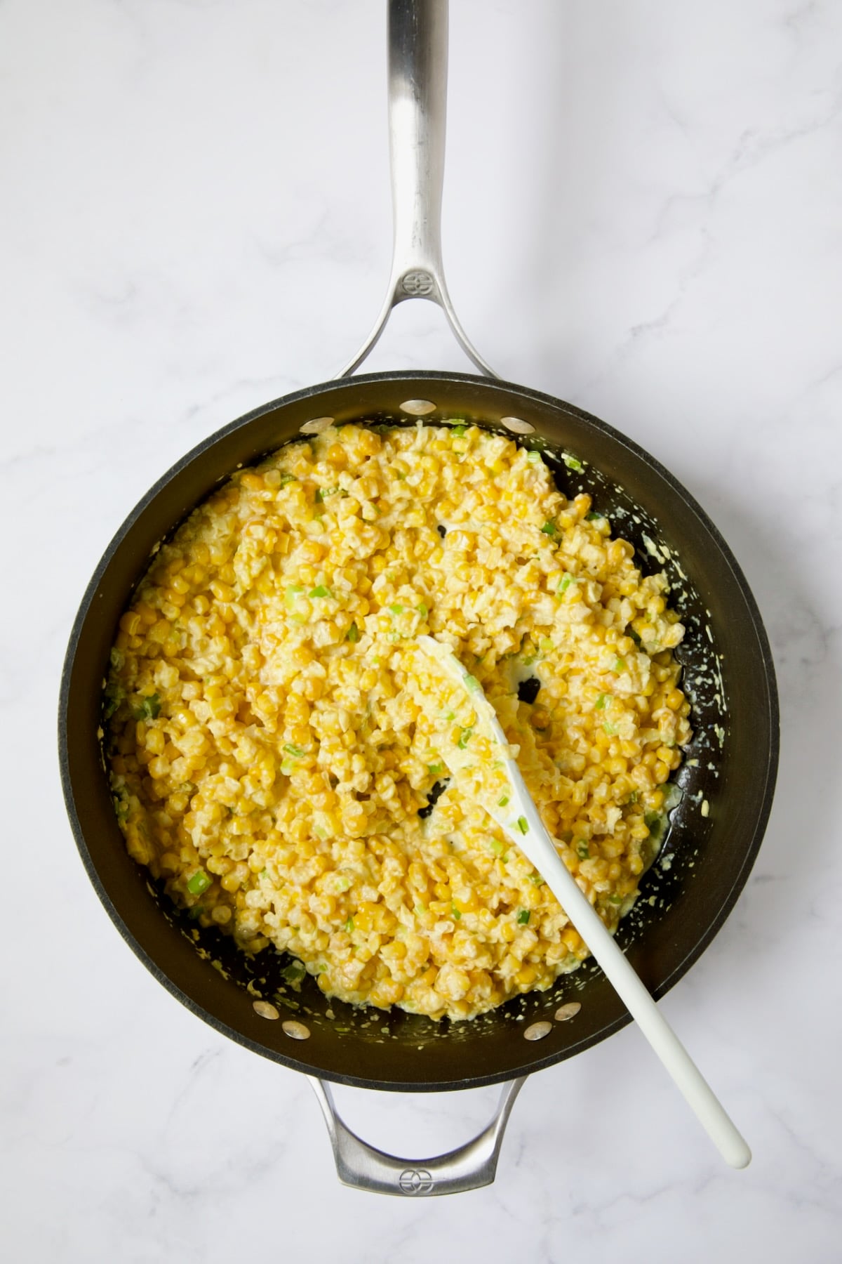 Corn in nonstick skillet being stirred with white spoon.