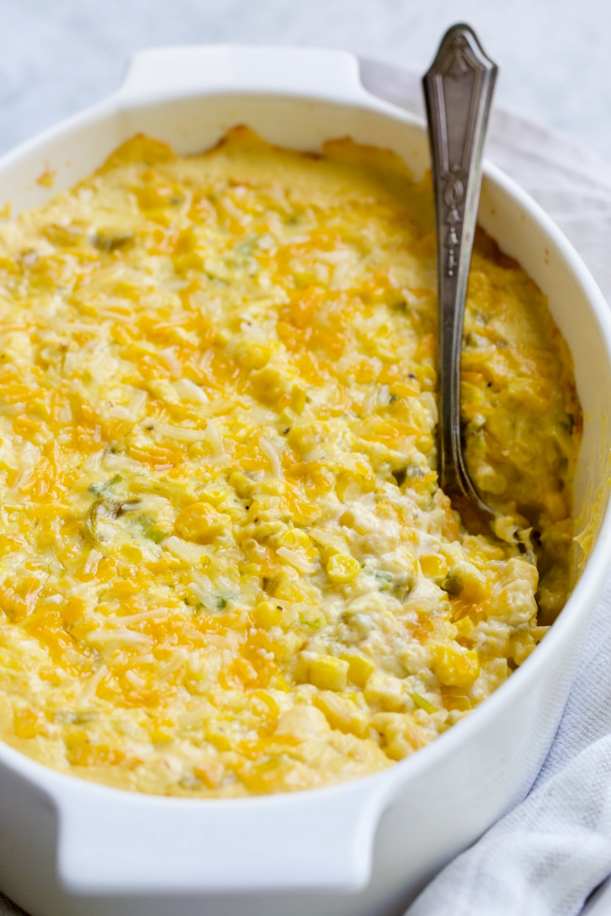 Cream Cheese Corn Casserole with Green Chiles in white oval baking dish with some scooped out.