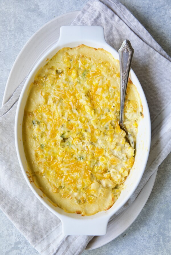 Cream Cheese Corn Casserole with Green Chiles in white oval baking dish with serving spoon.