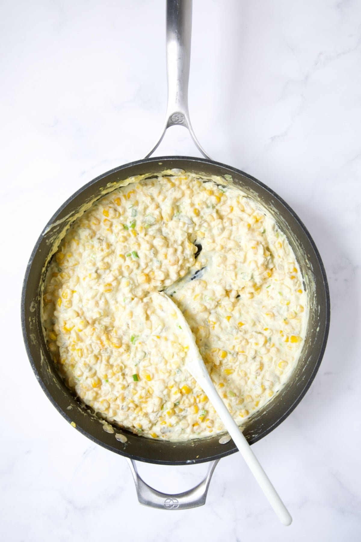 Corn casserole with cream cheese and green chiles blended in being stirred with white spoon.