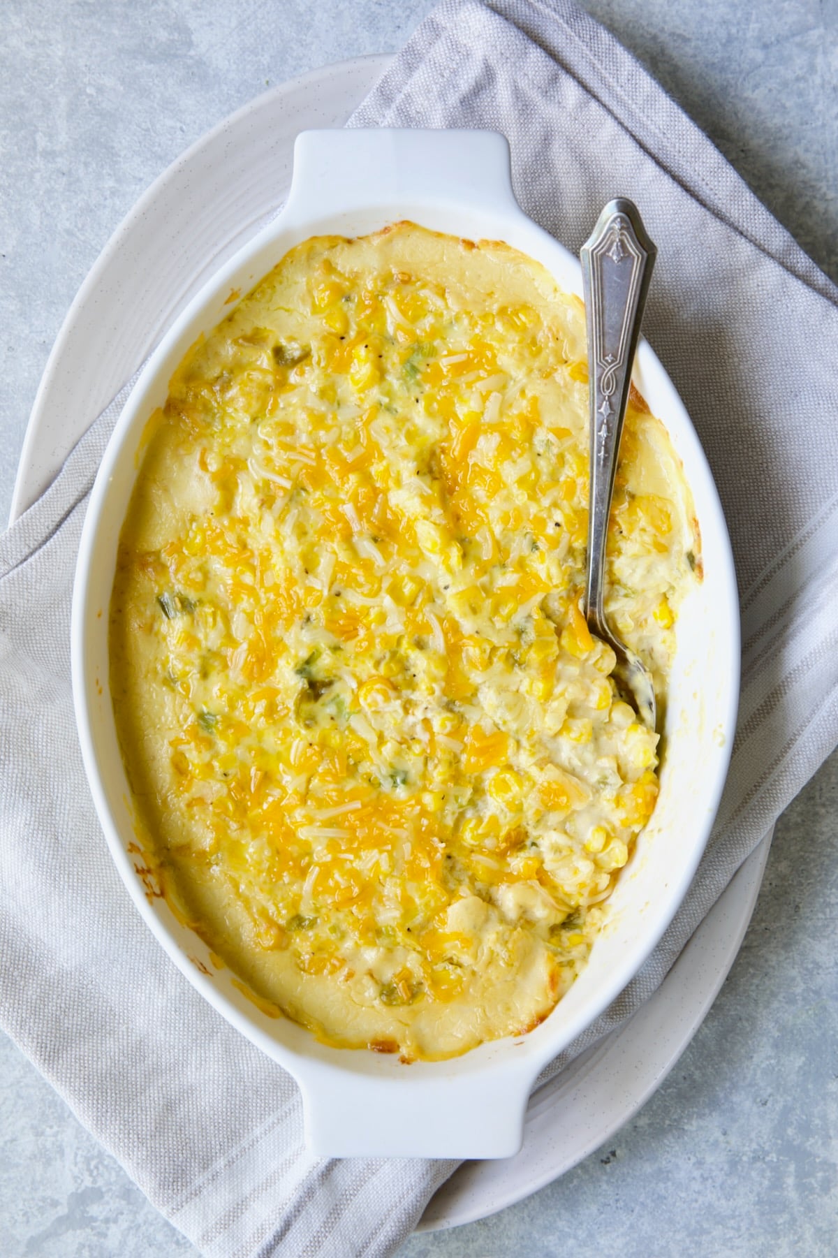 Cream Cheese Corn Casserole with Green Chiles in white oval baking dish with serving spoon.
