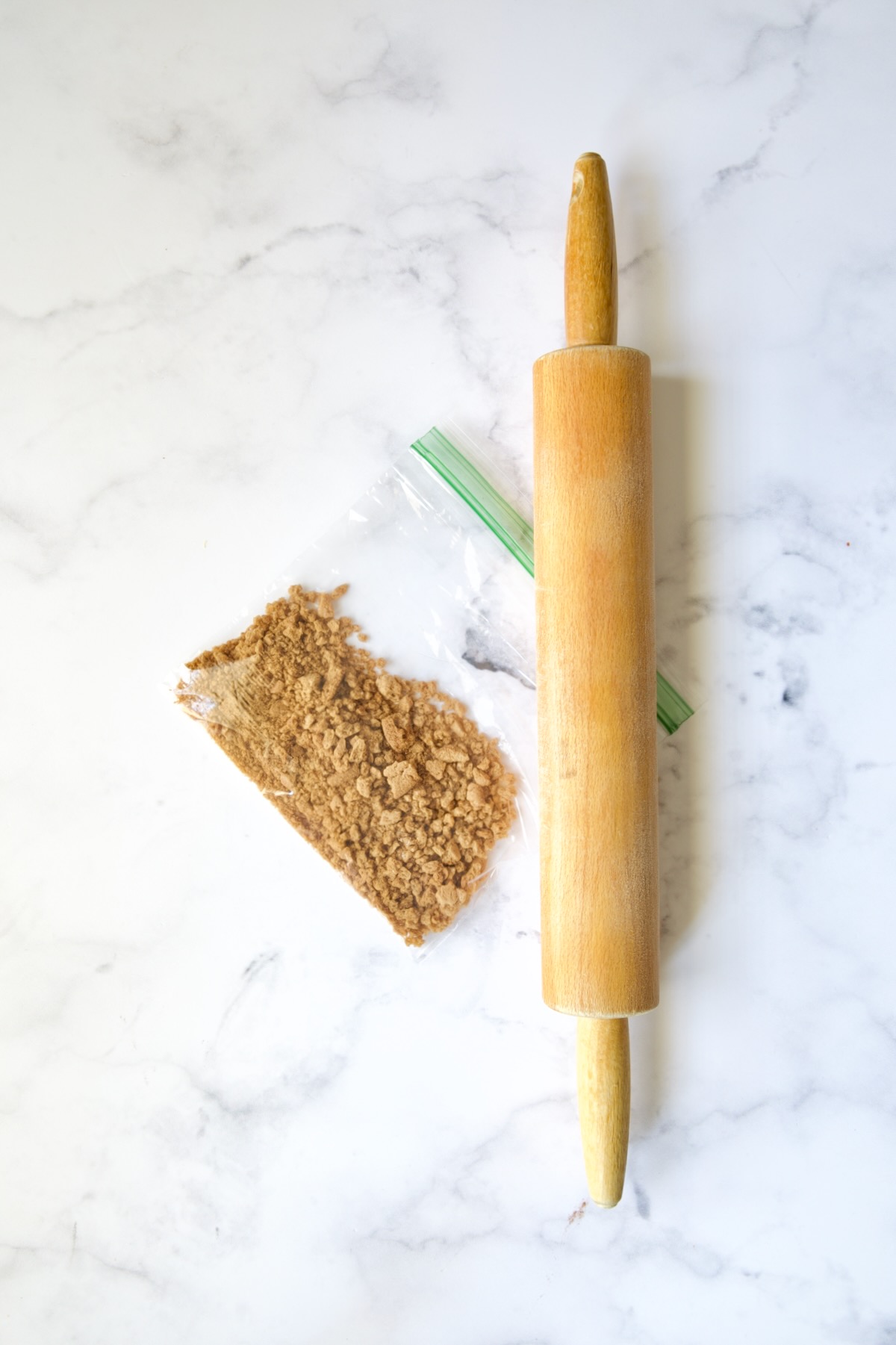 Crushed gingersnap cookies in sandwich bag with rolling pin next to it.