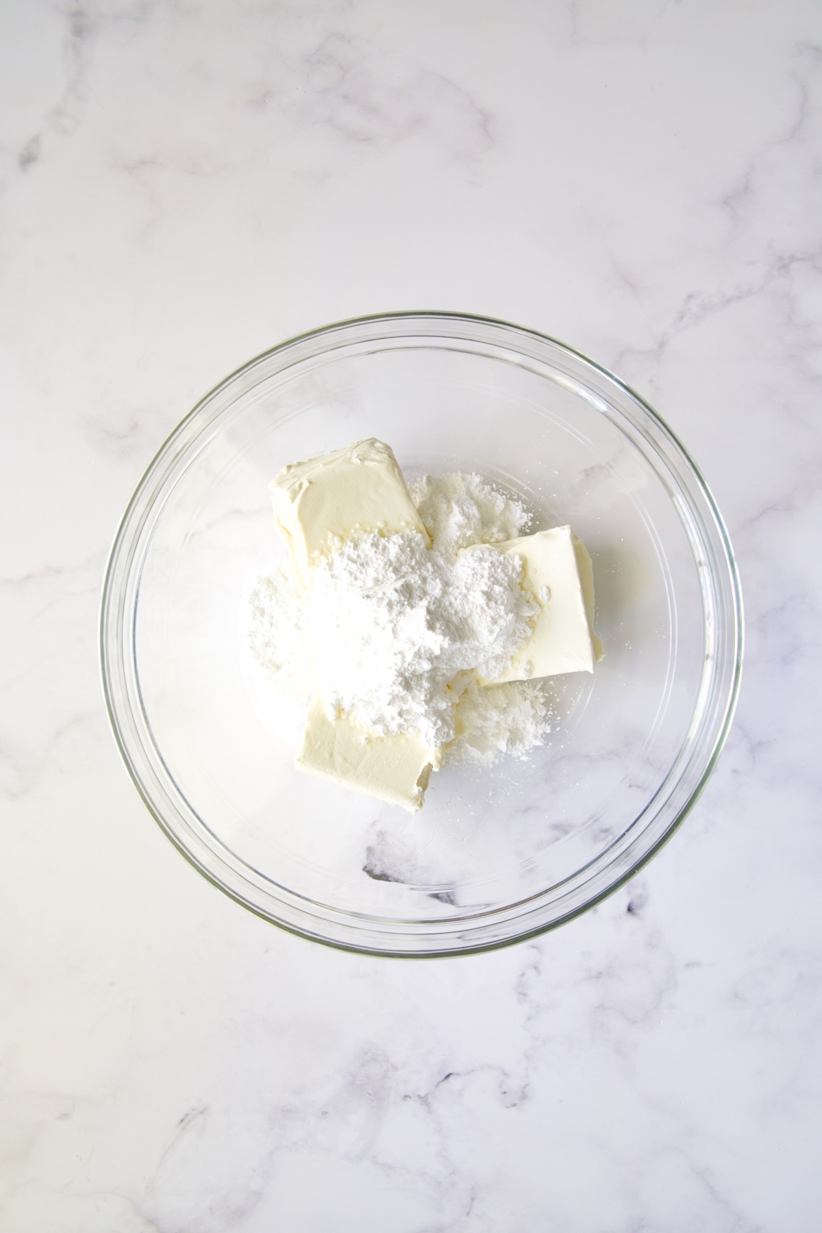 Cream cheese and powdered sugar in glass bowl.