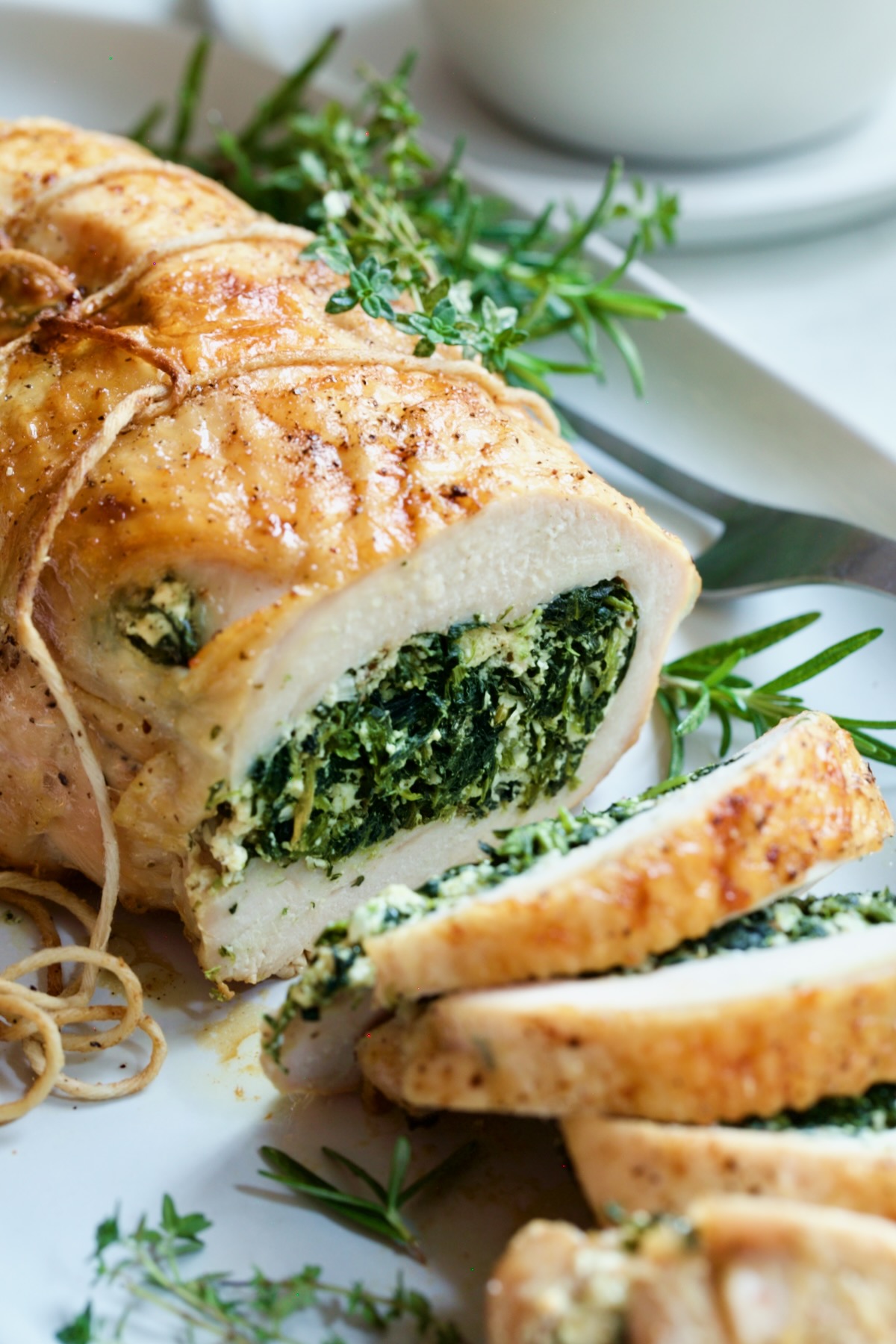 Spinach and Ricotta Stuffed Turkey Breast with Garlic - Herb Sauce garnished with fresh herbs on white platter.