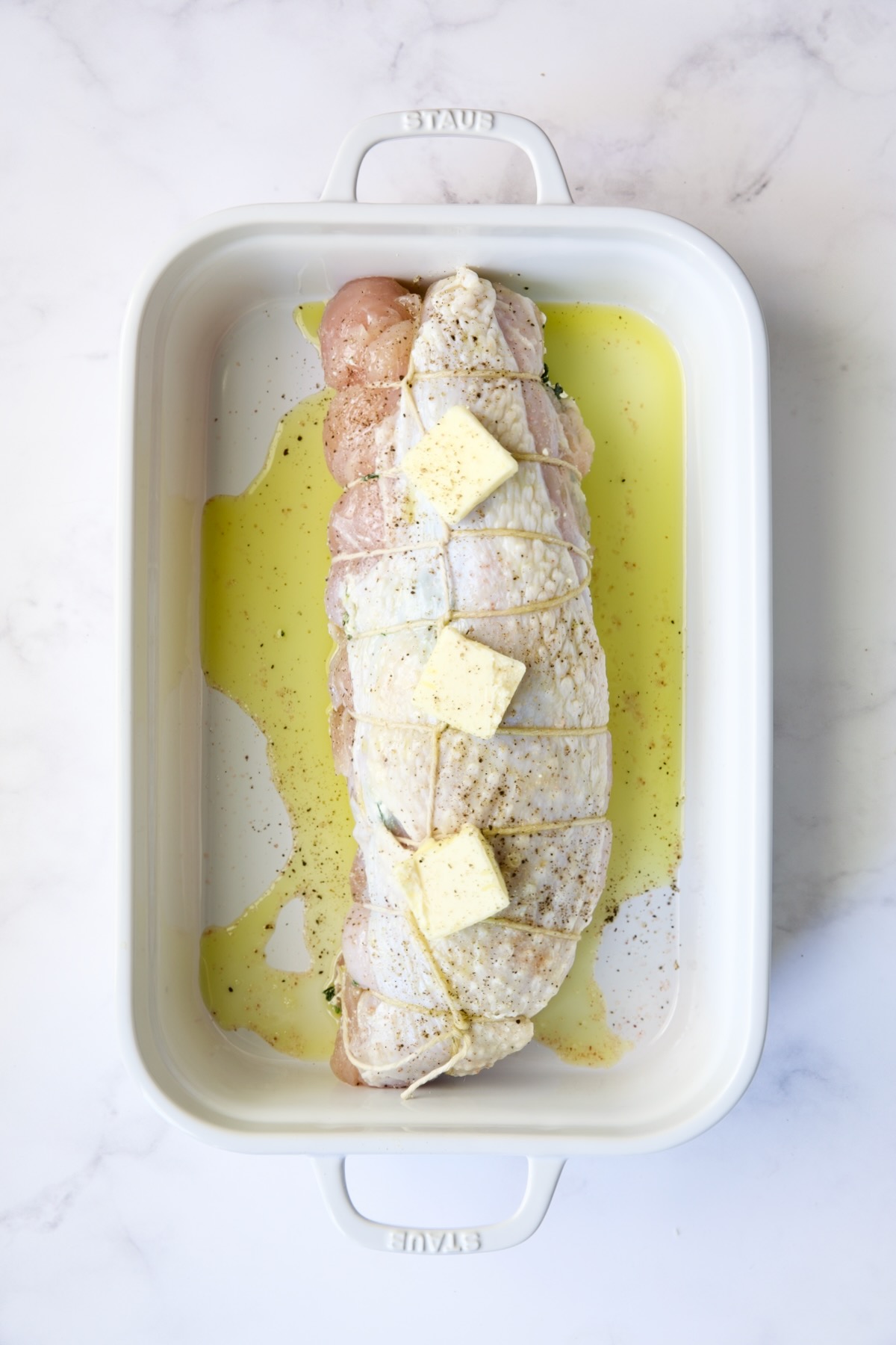 Uncooked stuffed turkey breast with olive oil drizzled over and topped with butter.