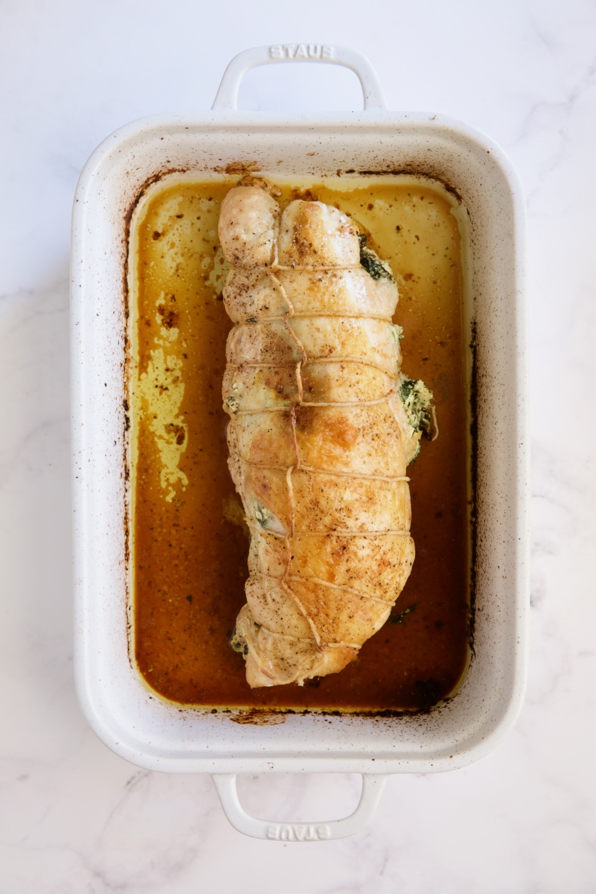 Cooked turkey breast in white roasting pan.