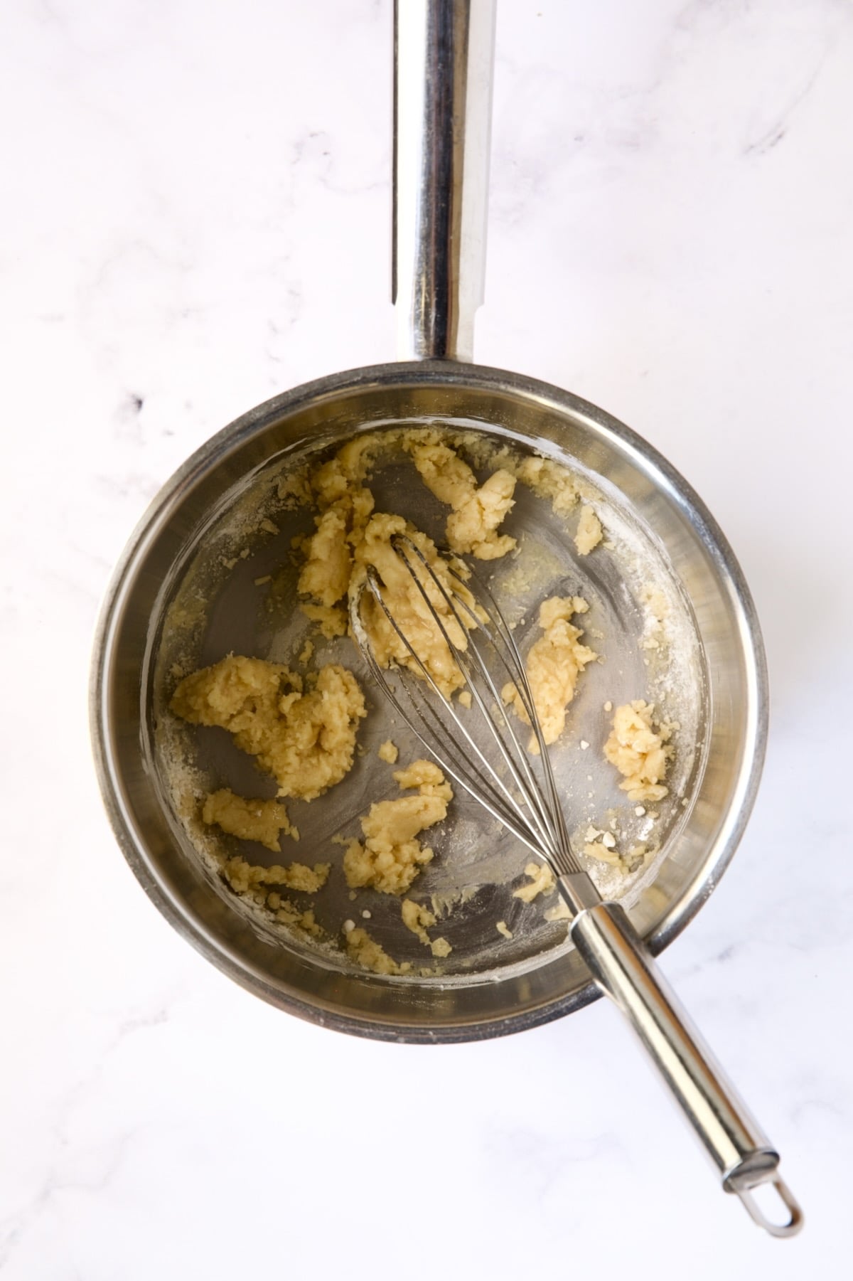 Wire whisk stirring flour and butter combination in stainless steel saucepan.