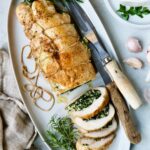 Spinach and Ricotta Stuffed Turkey Breast with Garlic - Herb Sauce on white oval platter garnished with fresh herbs.