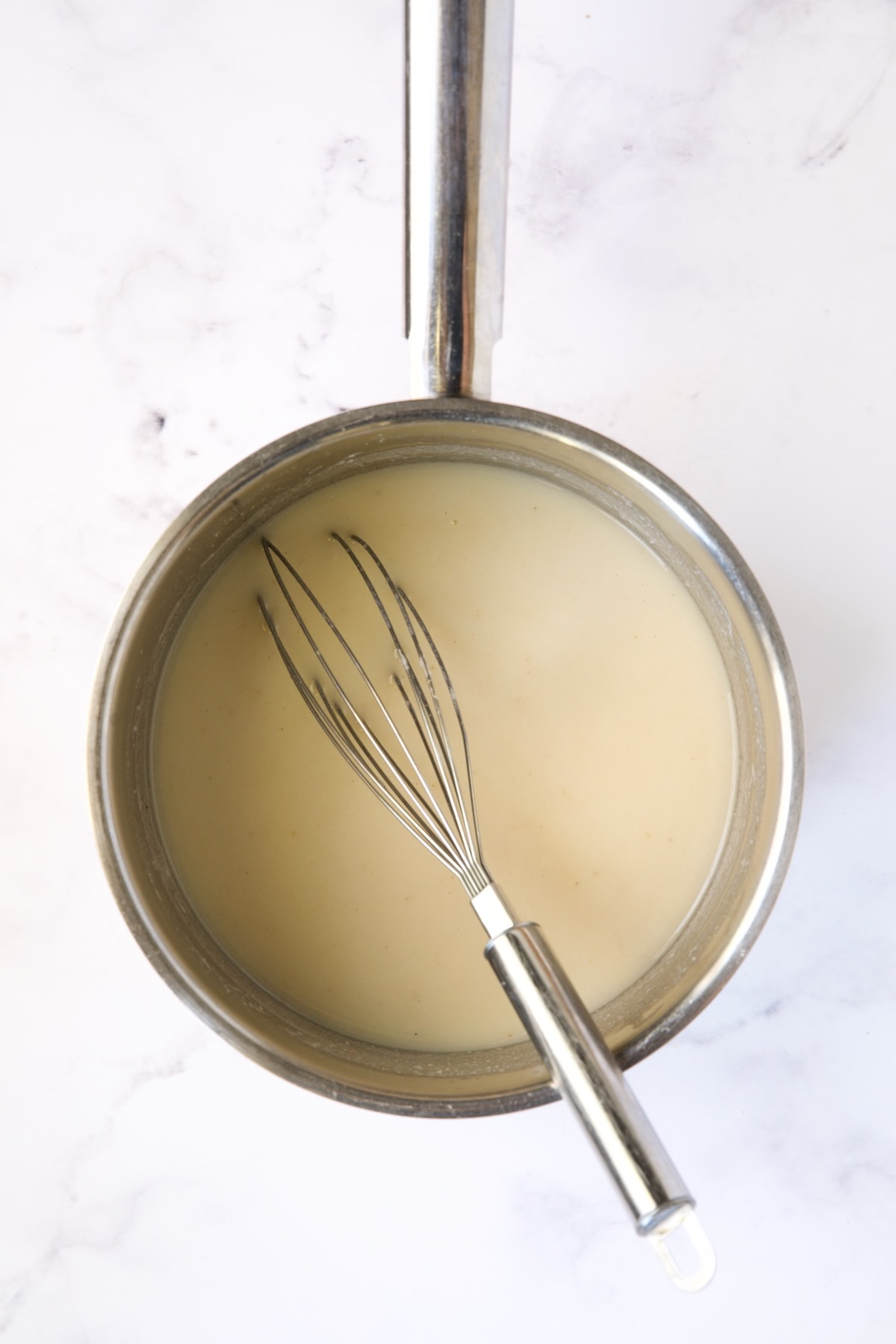 Sauce in stainless steel saucepan with broth added.