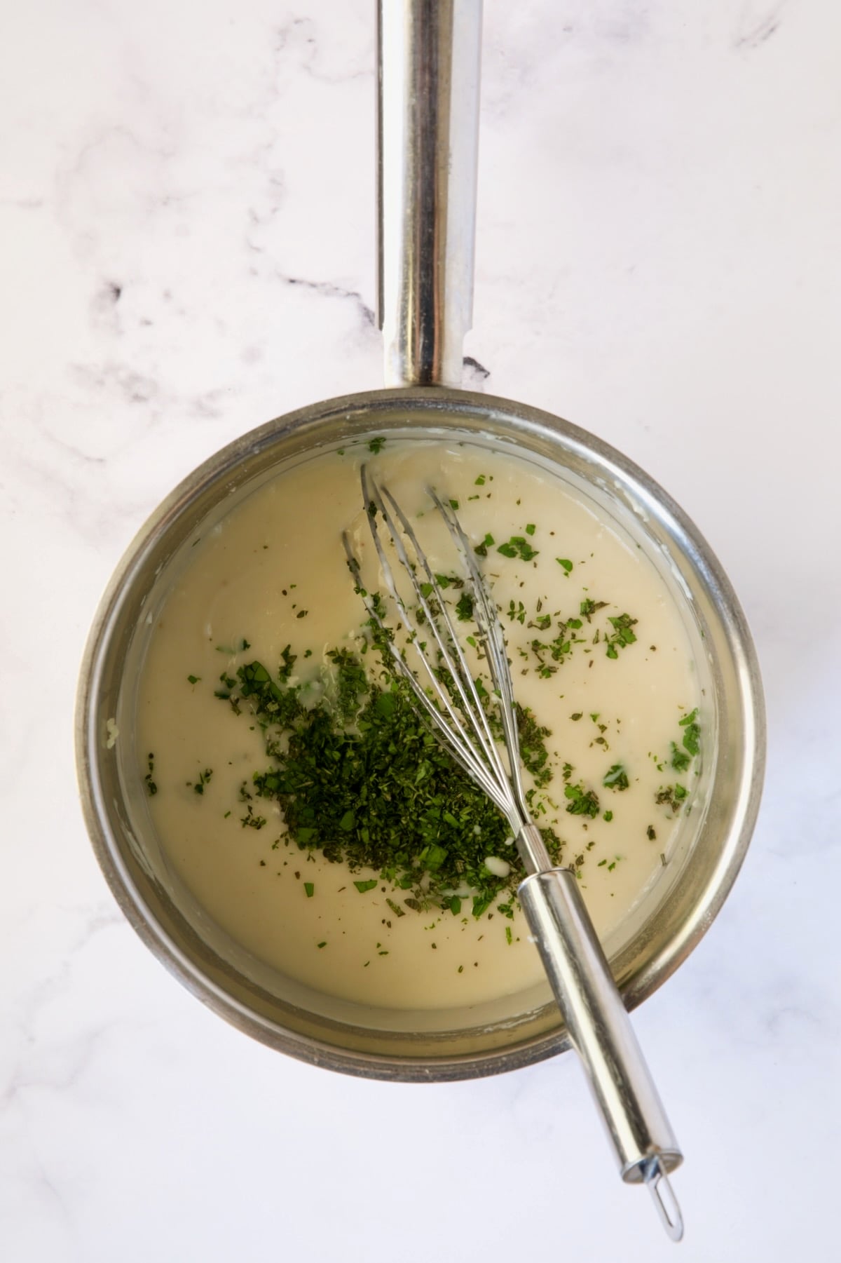 Sauce in stainless steel skillet with fresh herbs added.