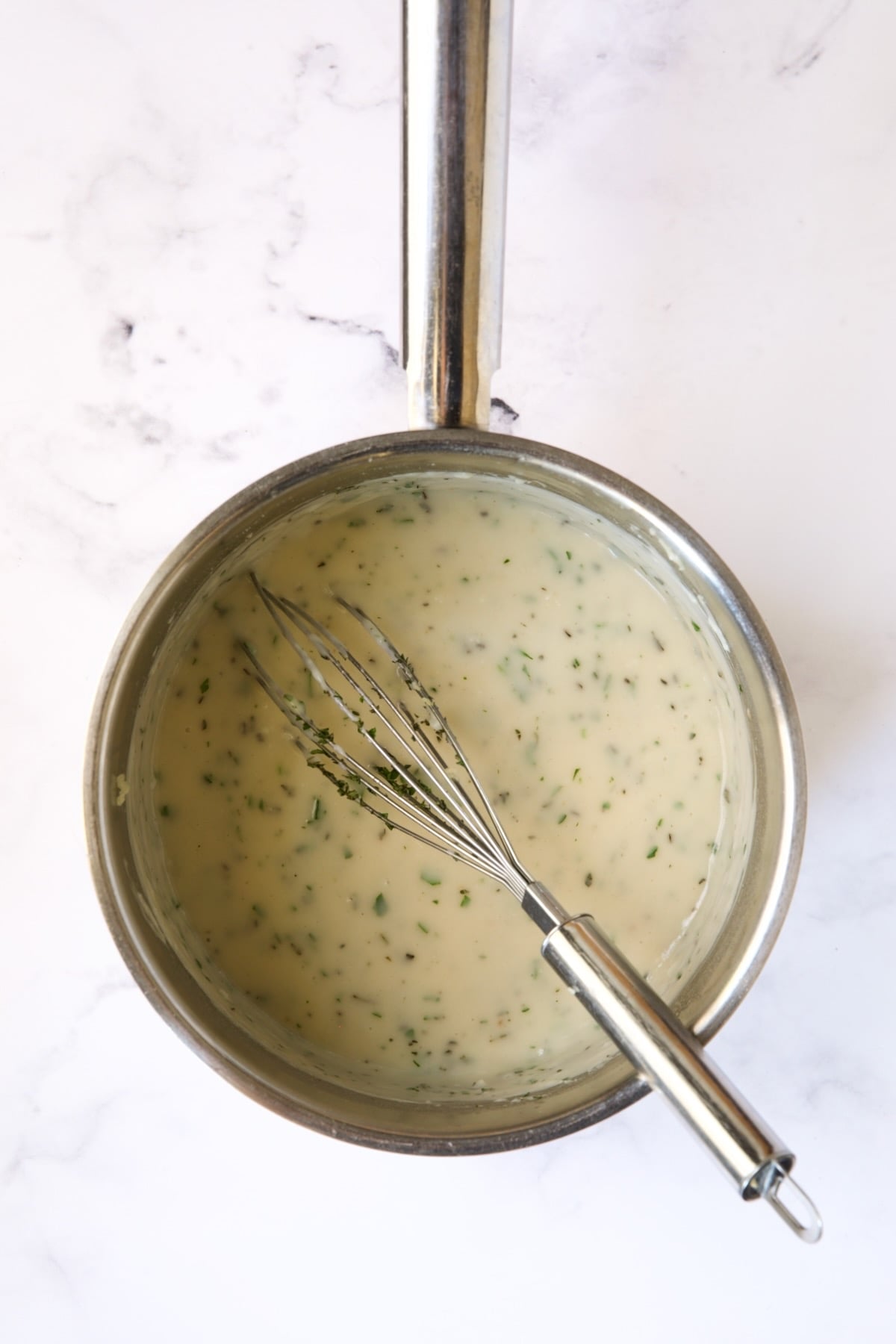 Sauce in stainless steel saucepan with whisk.