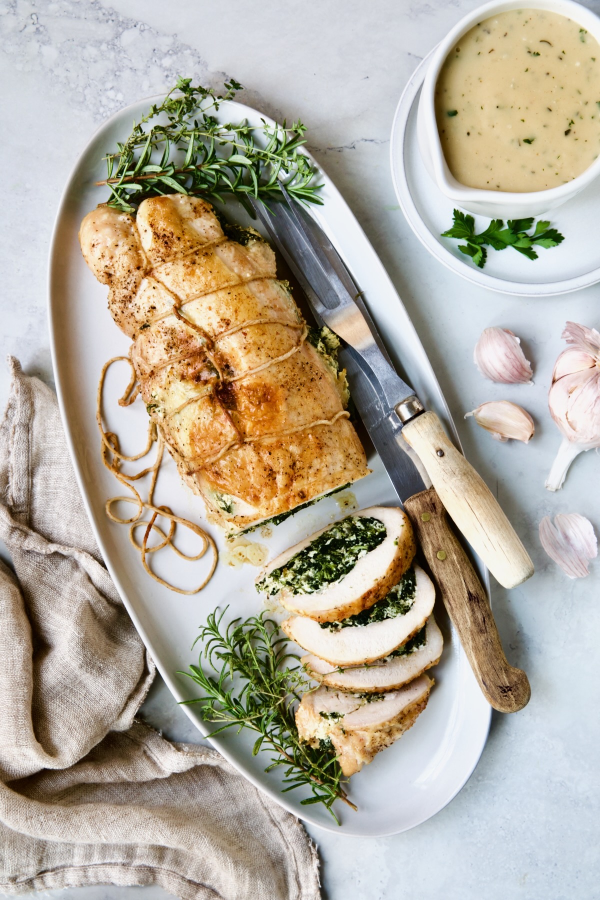Spinach and Ricotta Stuffed Turkey Breast with Garlic - Herb Sauce on white oval platter with serving utensils.