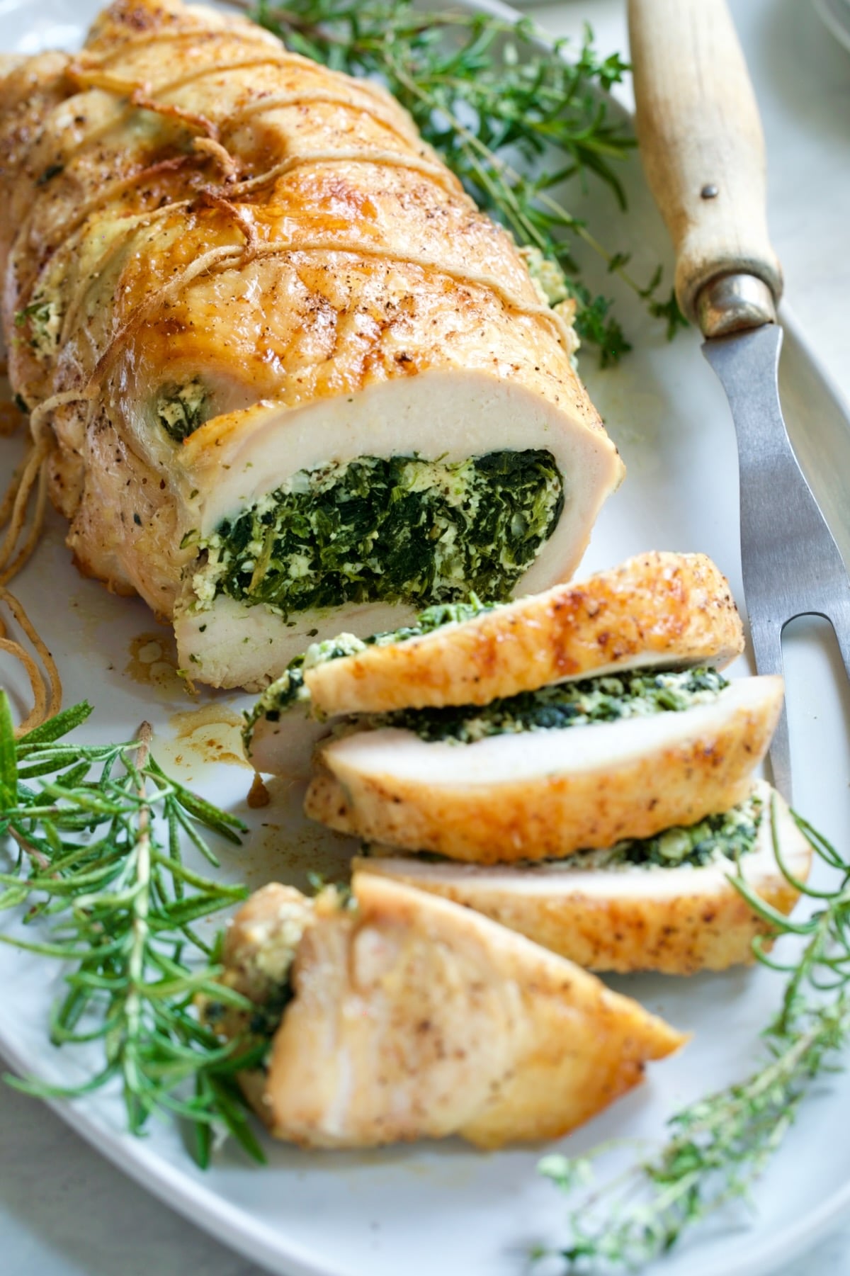 Spinach and Ricotta Stuffed Turkey Breast with Garlic - Herb Sauce on white platter with serving fork.