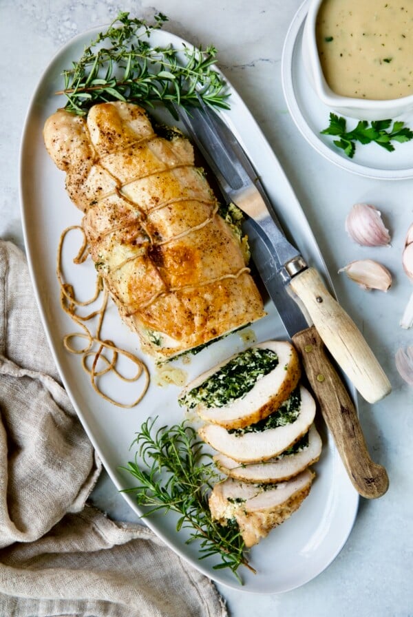 Spinach and Ricotta Stuffed Turkey Breast with Garlic - Herb Sauce on white oval platter garnished with fresh herbs.