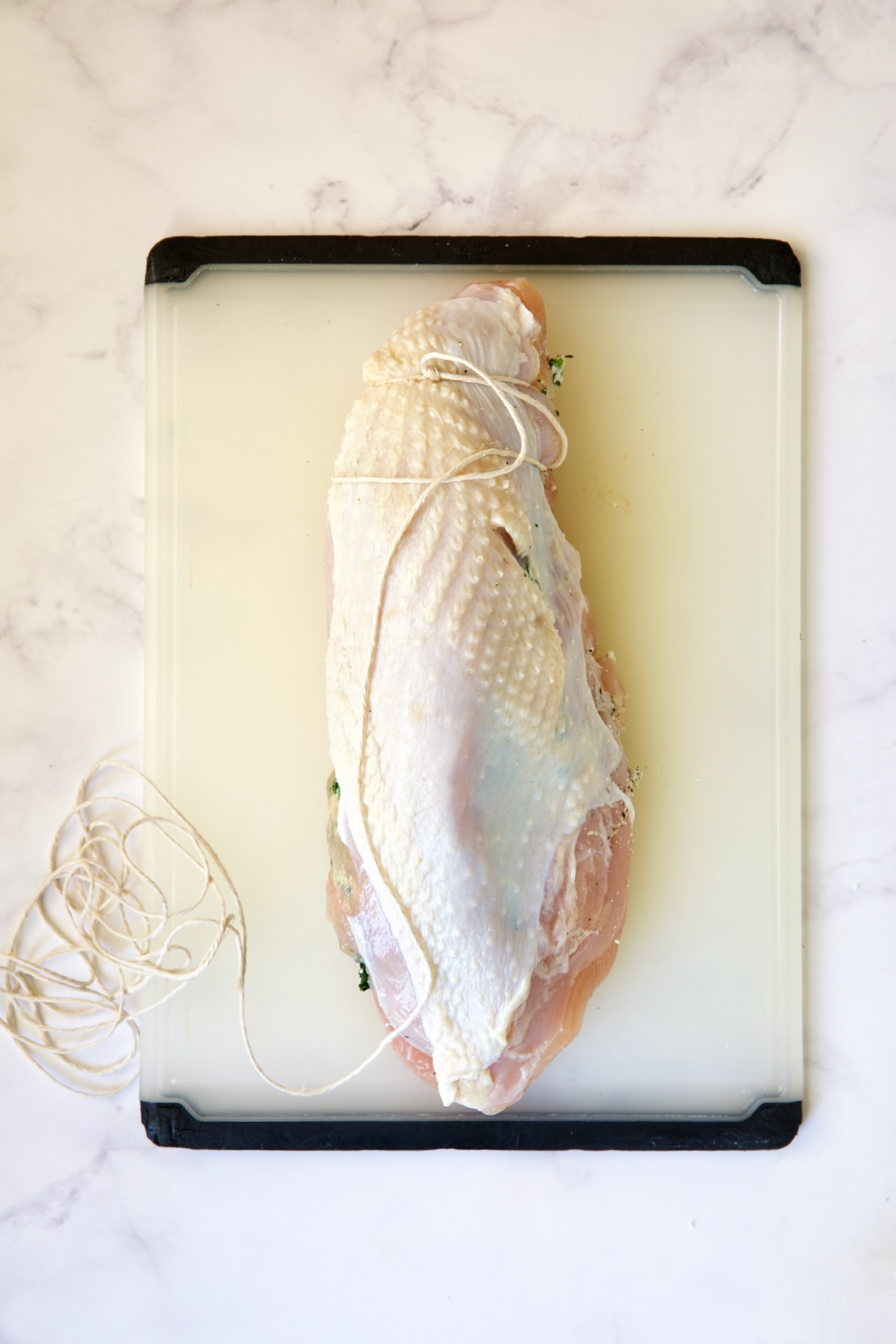 Stuffed turkey breast being tied on white plastic cutting board.