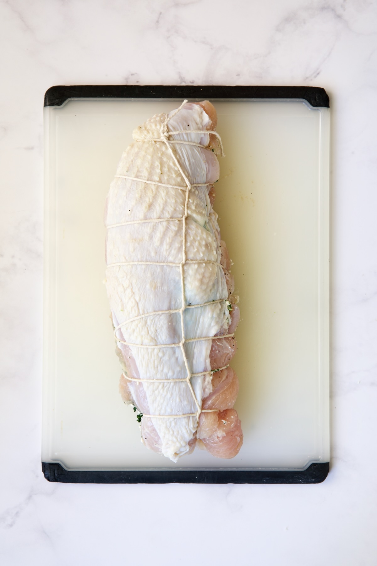 Tied uncooked stuffed turkey breast on white plastic cutting board.