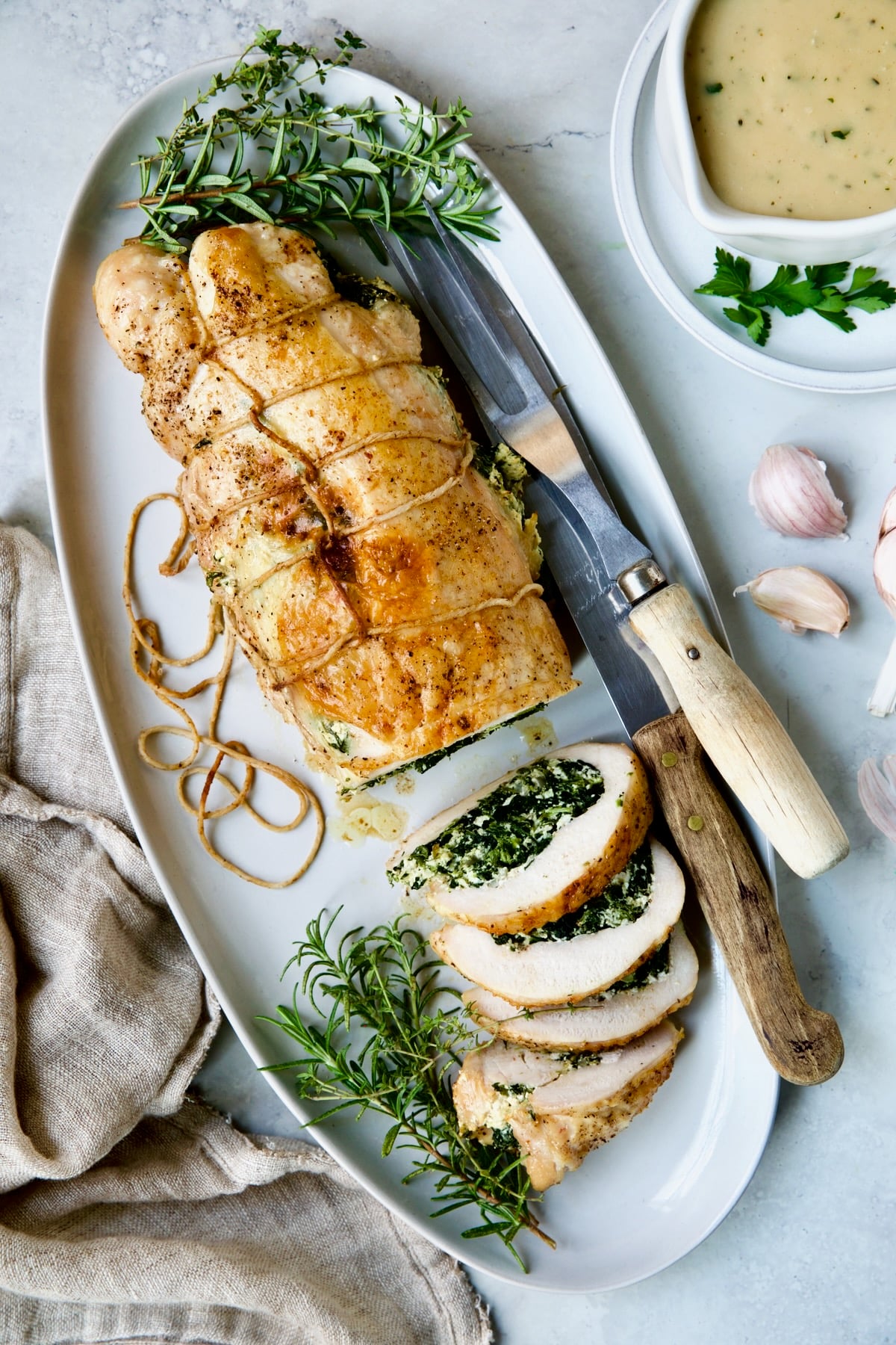Spinach and Ricotta Stuffed Turkey Breast with Garlic - Herb Sauce on white oval platter garnished with fresh herbs.