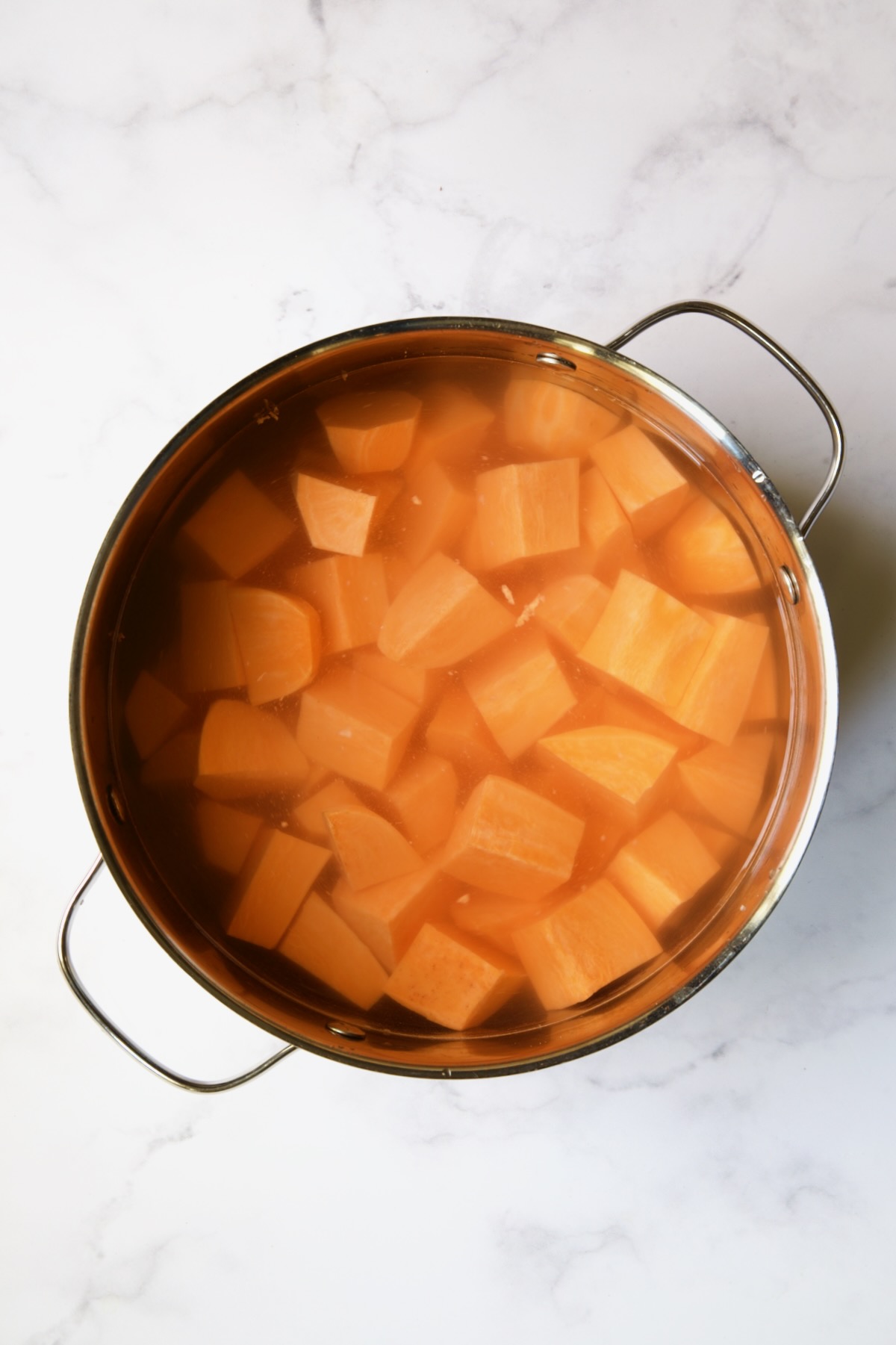 Uncooked sweet potatoes in stainless steel pot covered with water.