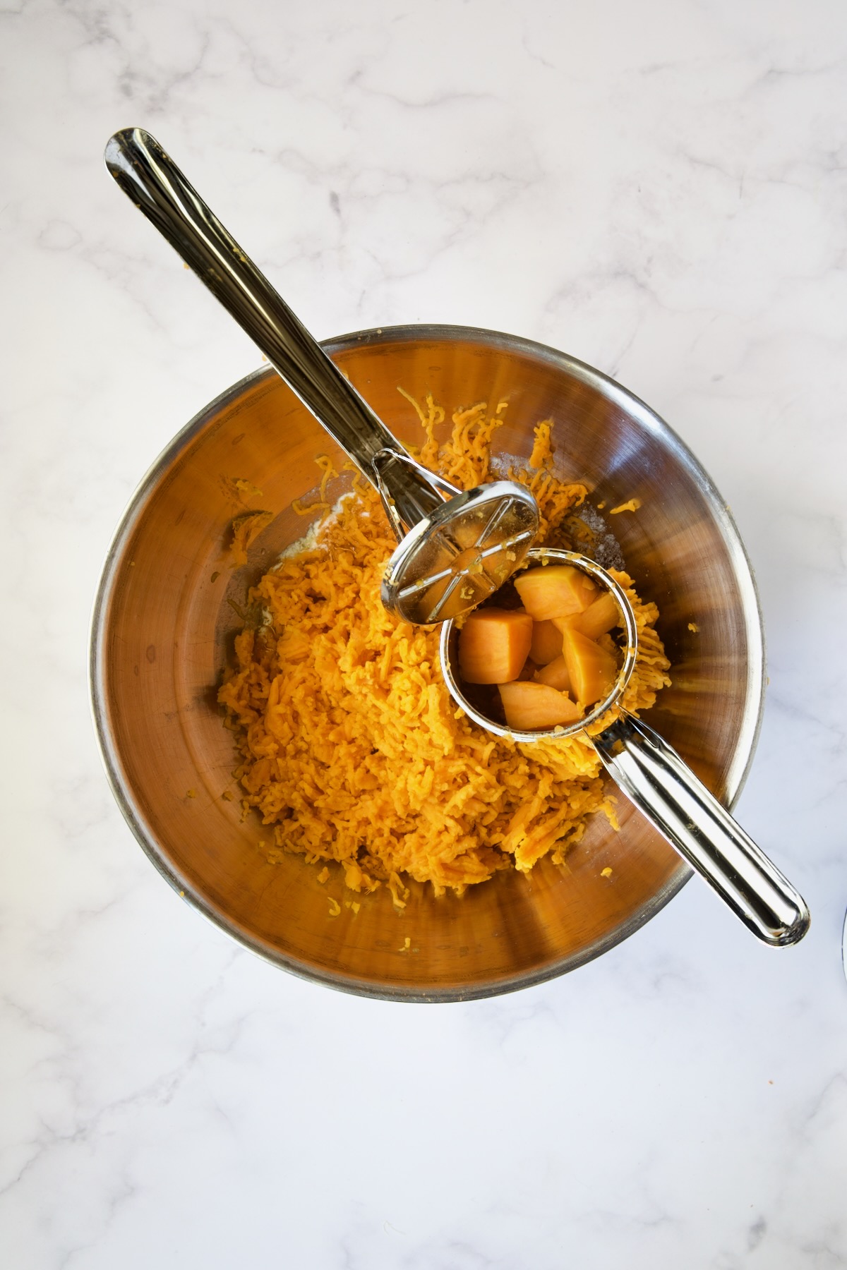 Sweet potatoes being processed through ricer in stainless steel bowl.