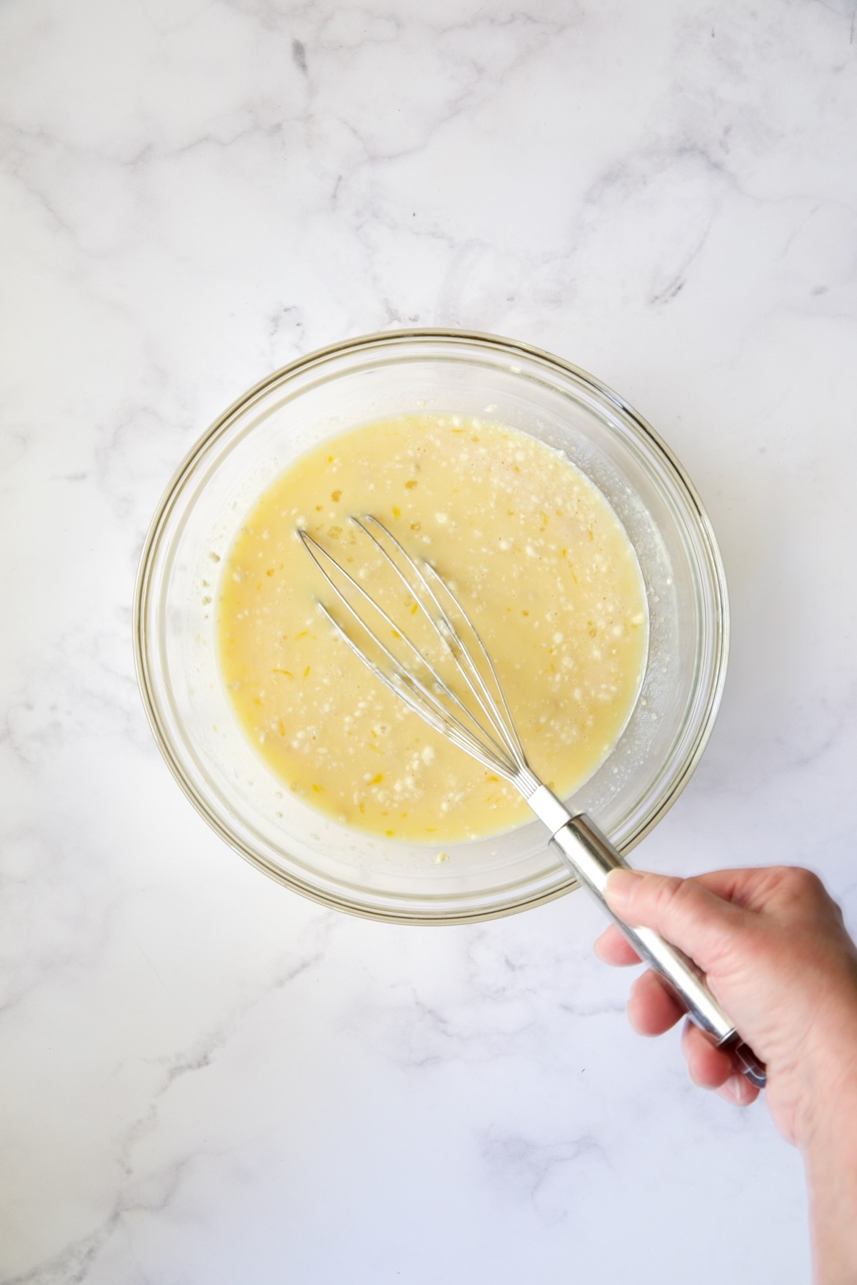 Egg, milk, flour and extract mixture being whisked in glass bowl.