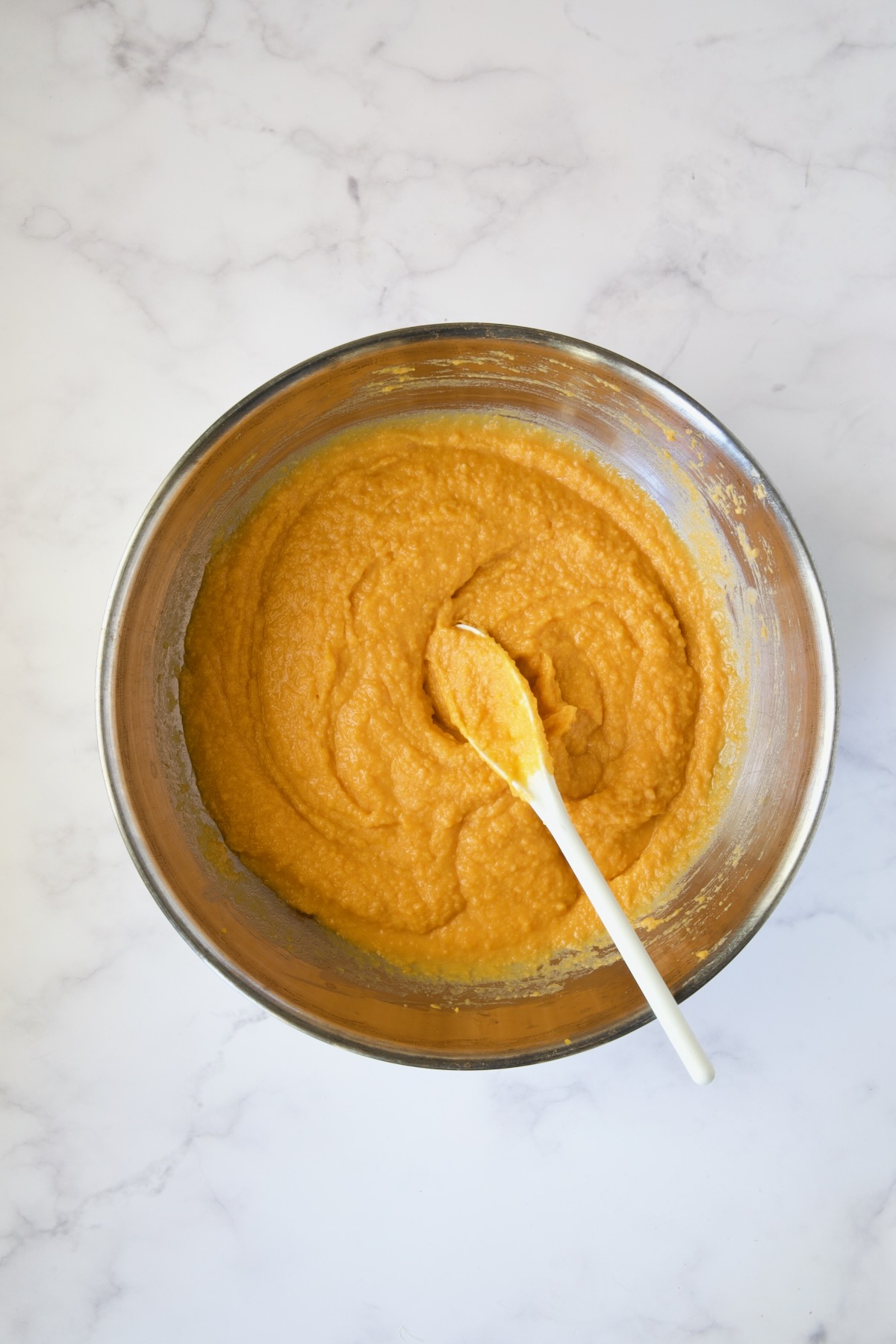 Sweet potato combination in stainless steel mixing bowl with white spoon.