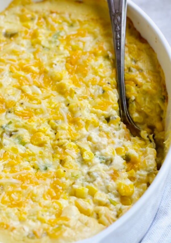 Cream Cheese Corn Casserole with Green Chiles in white oval baking dish with serving spoon.