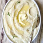 Creamy Turnip Potato Puree in white oval bowl with serving spoon on napkin with red stripe.