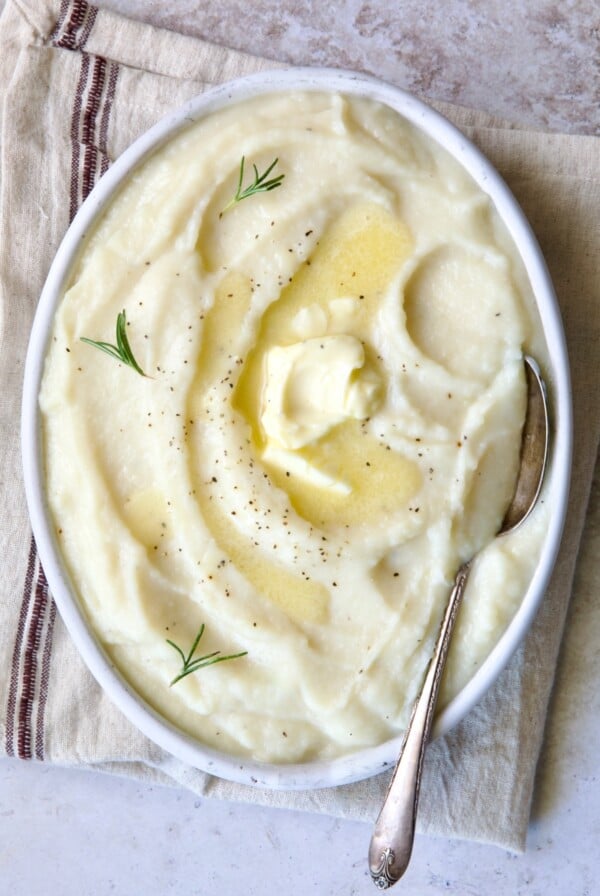 Creamy Turnip Potato Puree in white oval bowl with serving spoon on napkin with red stripe.