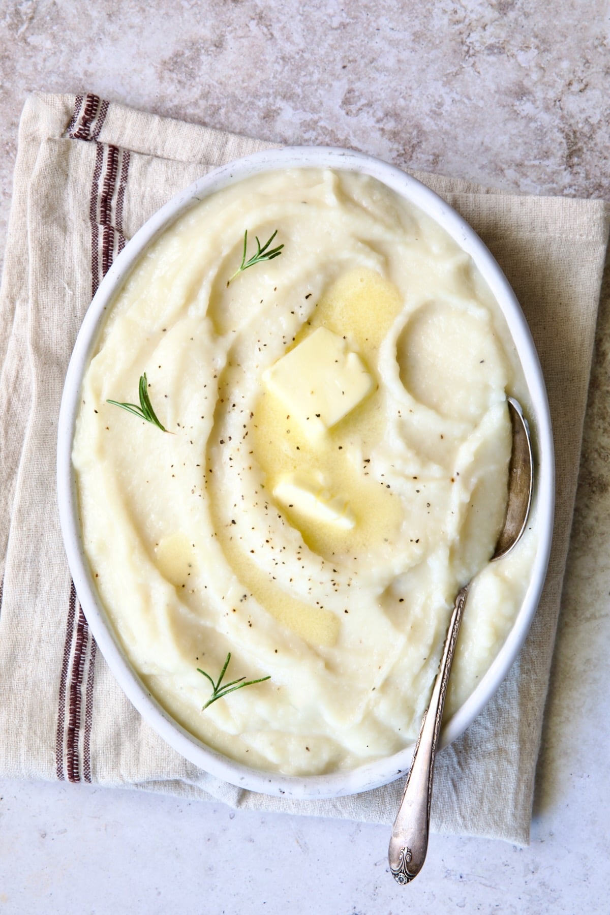 Creamy Mashed Turnip Recipe in white oval bowl with serving spoon on napkin with red stripe.
