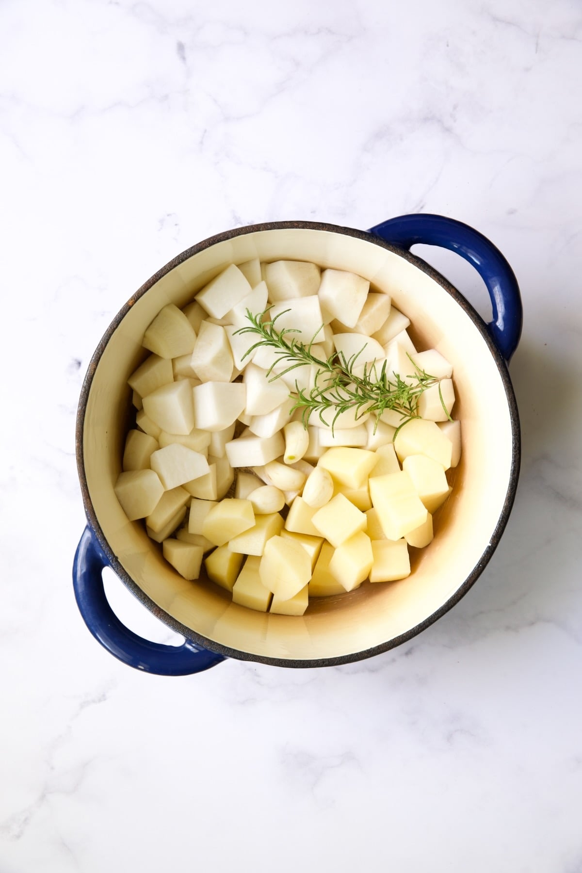 Cubed turnips, potatoes and a sprig of rosemary in blue Dutch oven.