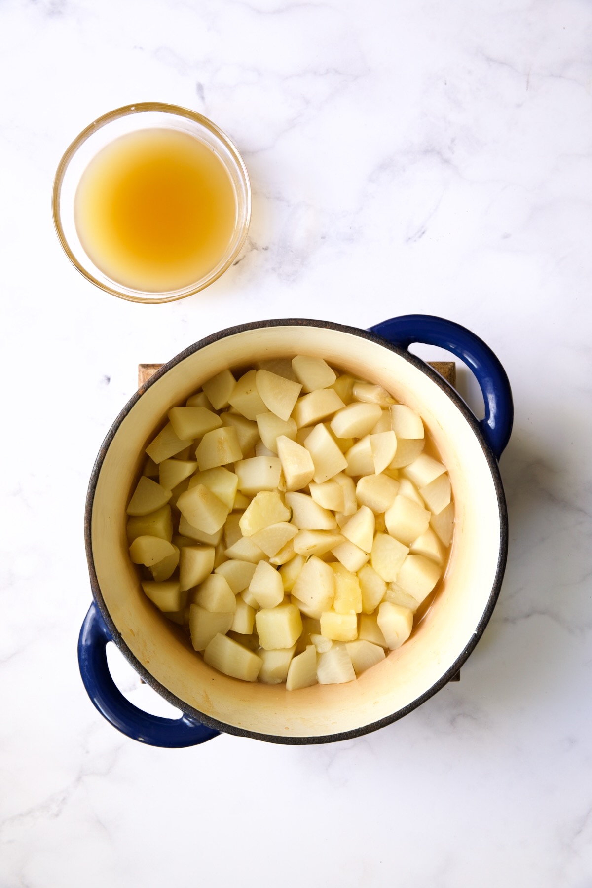 Cooked turnips and potatoes in blue Dutch oven with chicken broth drained out into a bowl.