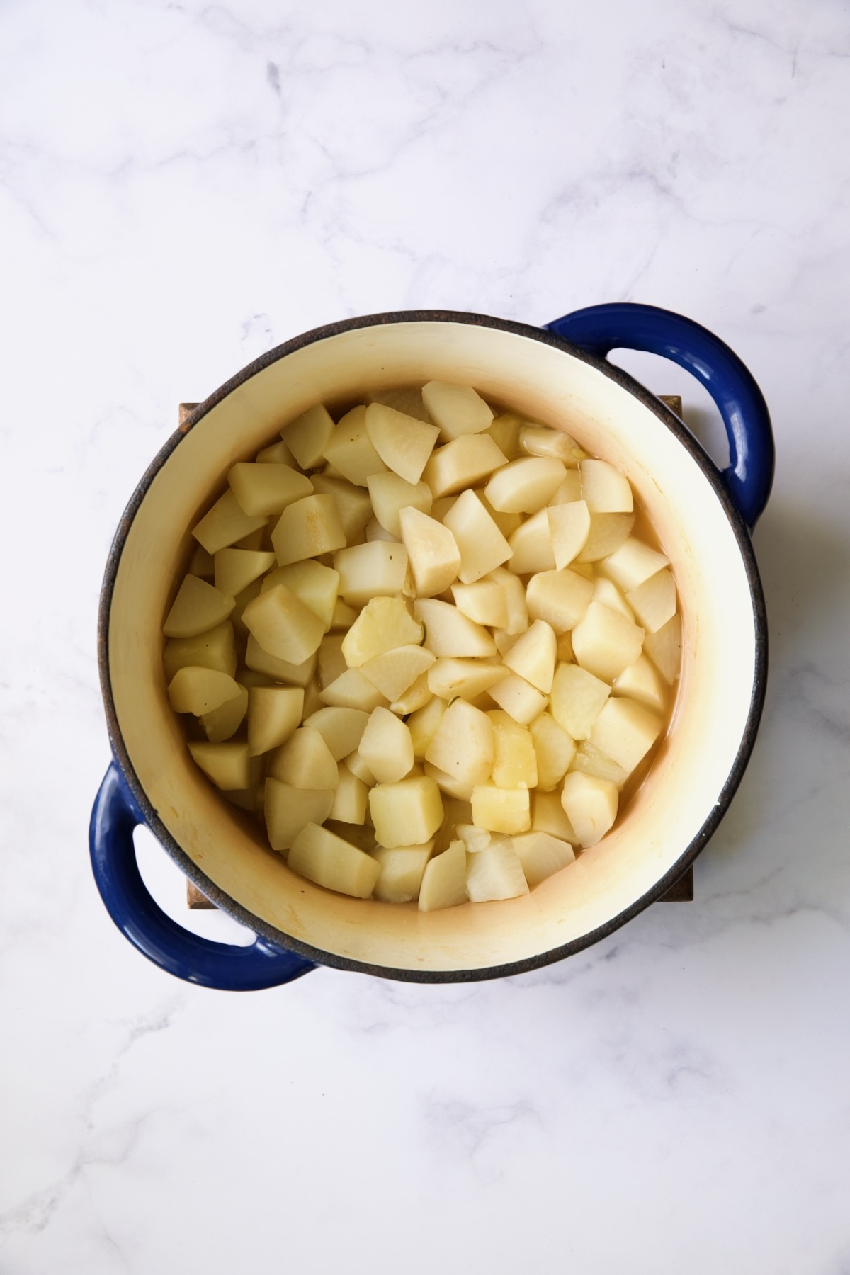 Cooked turnips and potatoes in blue Dutch oven with chicken broth drained out.