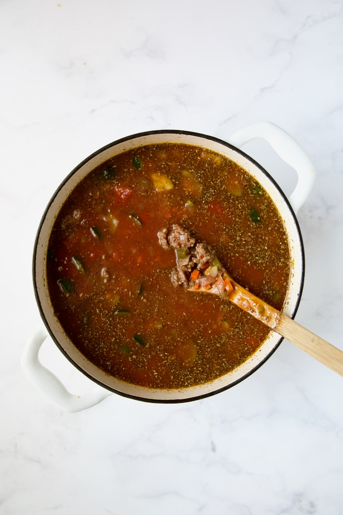 Wooden spoon stirring soup in white Dutch oven.