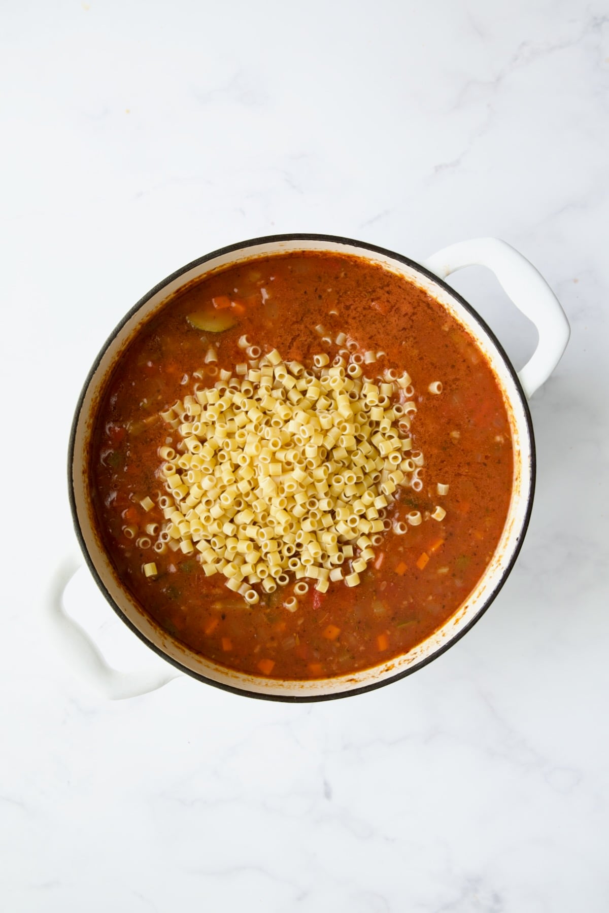 Pasta added to soup in white Dutch oven.