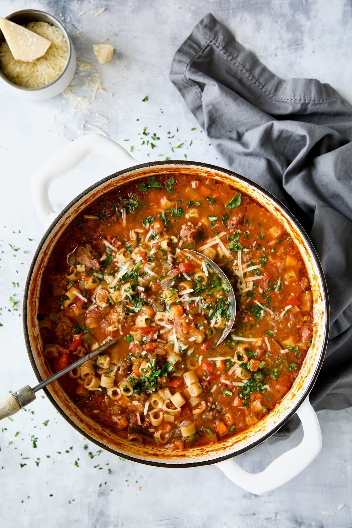 Italian Sausage Soup in white Dutch oven garnished with fresh parsley and Parmesan cheese.