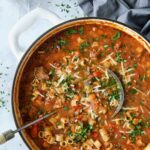 Italian Sausage Soup in white Dutch oven garnished with fresh parsley and Parmesan cheese.