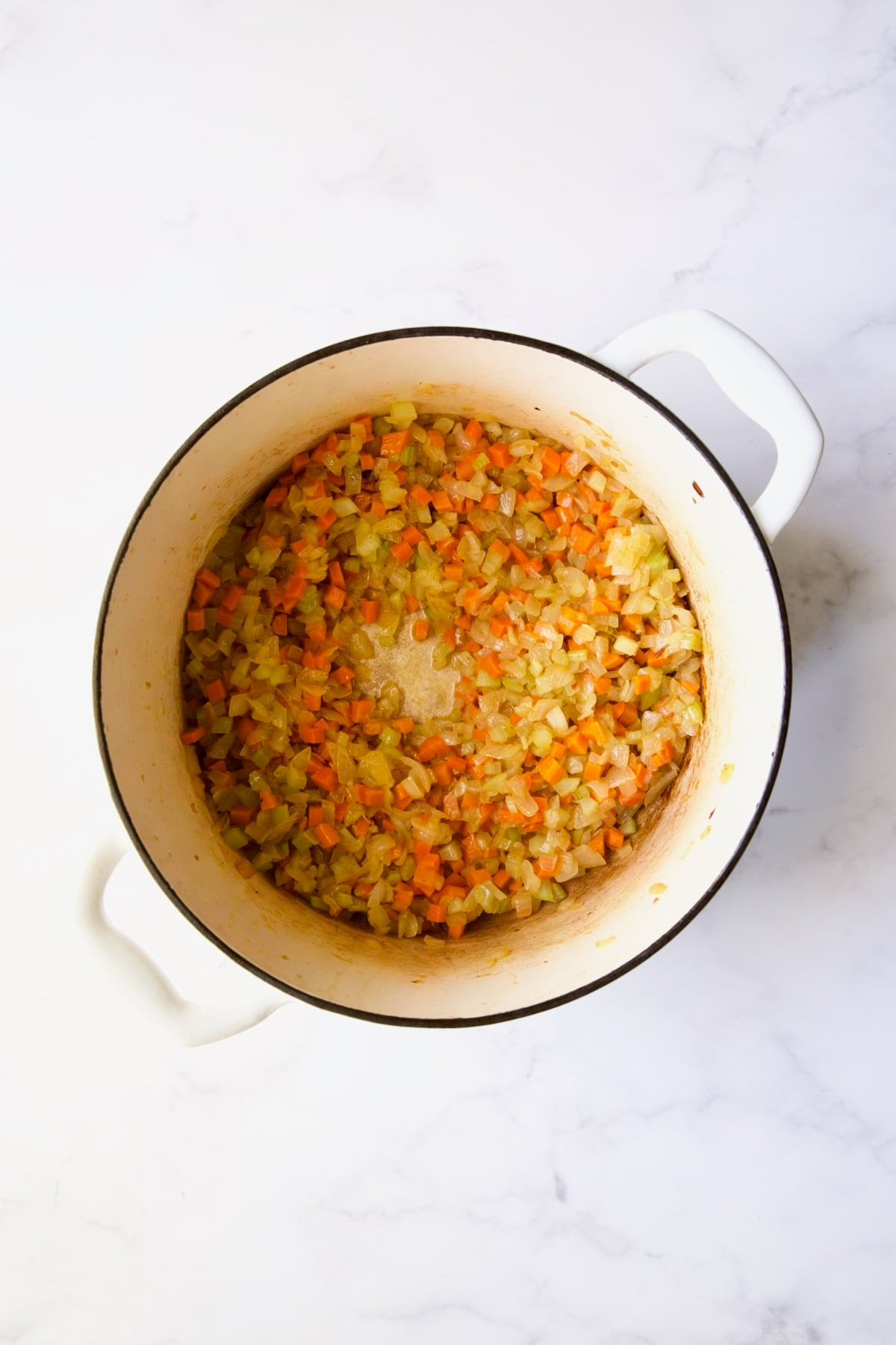 Cooked onion, celery and carrot in white Dutch oven.