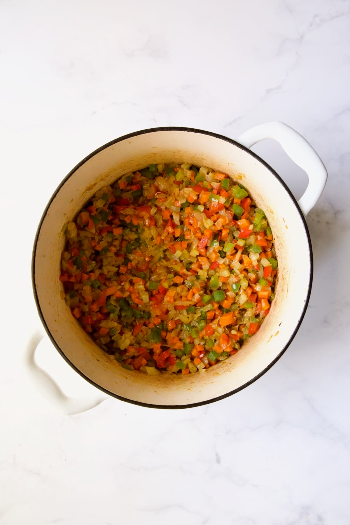Cooked onion, carrot, celery and bell peppers in white Dutch oven.