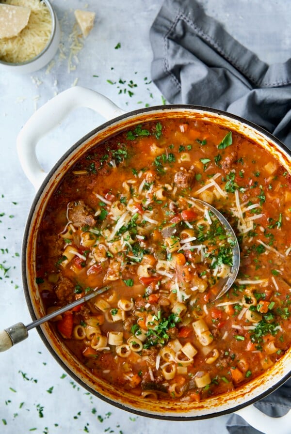 Italian Sausage Soup in white Dutch oven garnished with fresh parsley and Parmesan cheese.