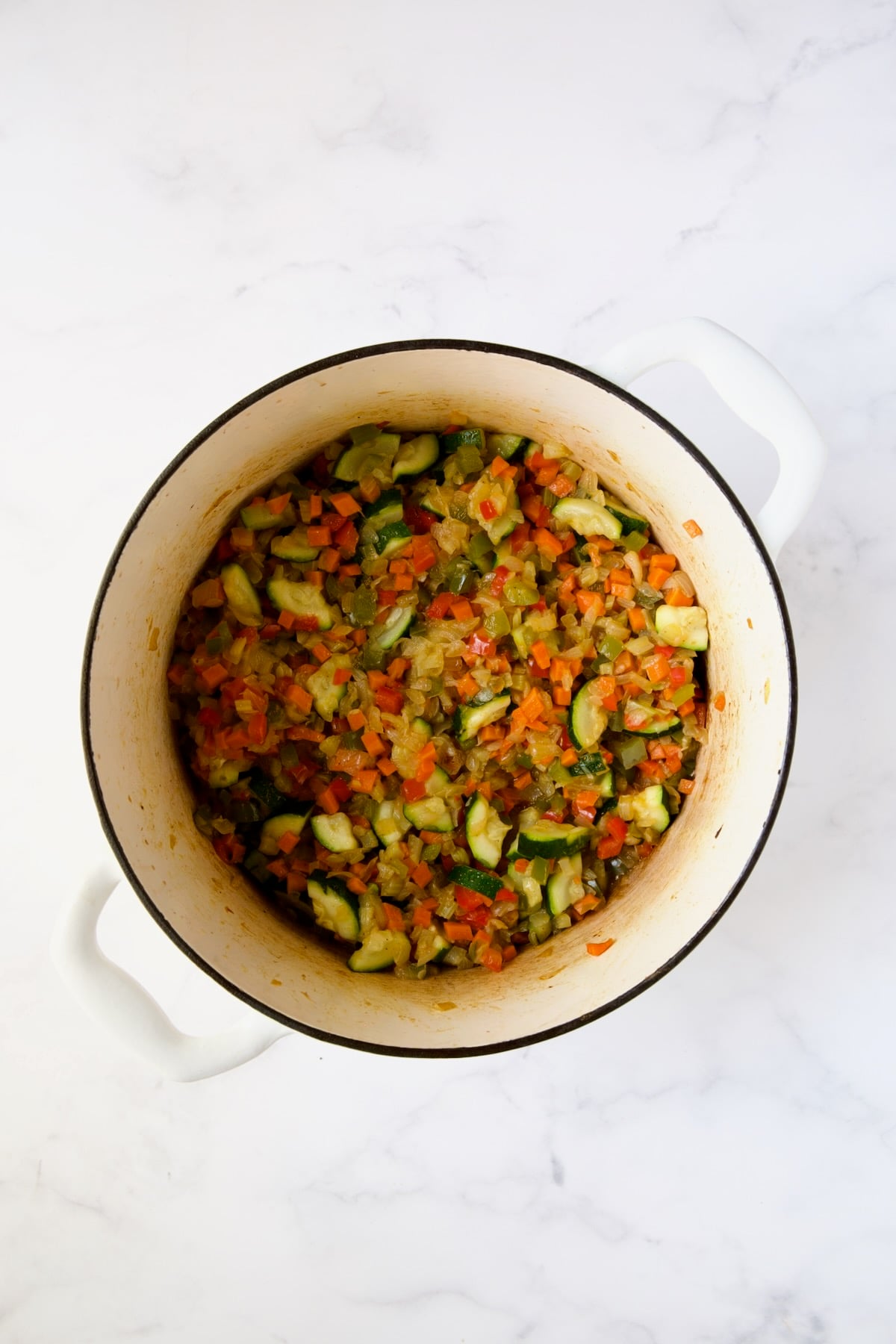 Cooked vegetables for soup in white Dutch oven.