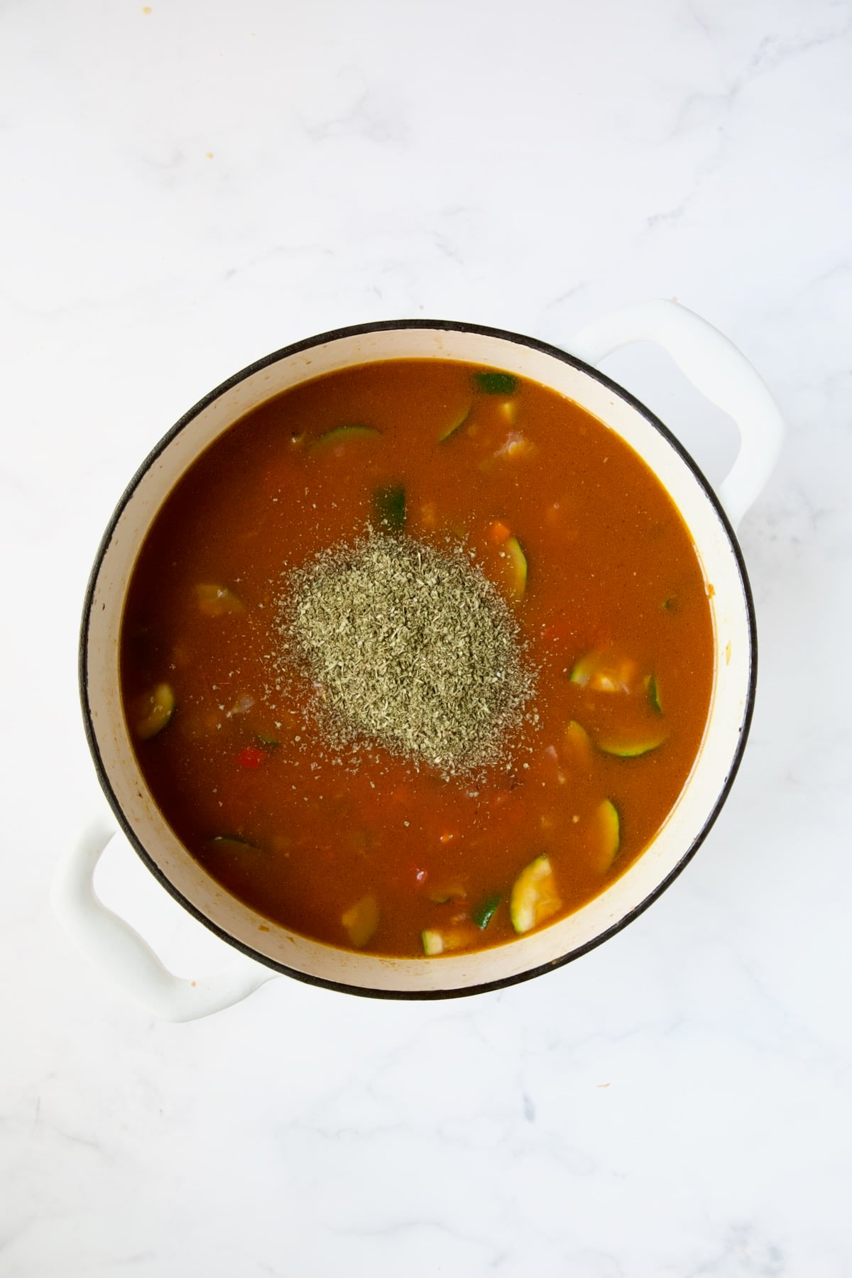 Italian seasoning added to soup in white Dutch oven.