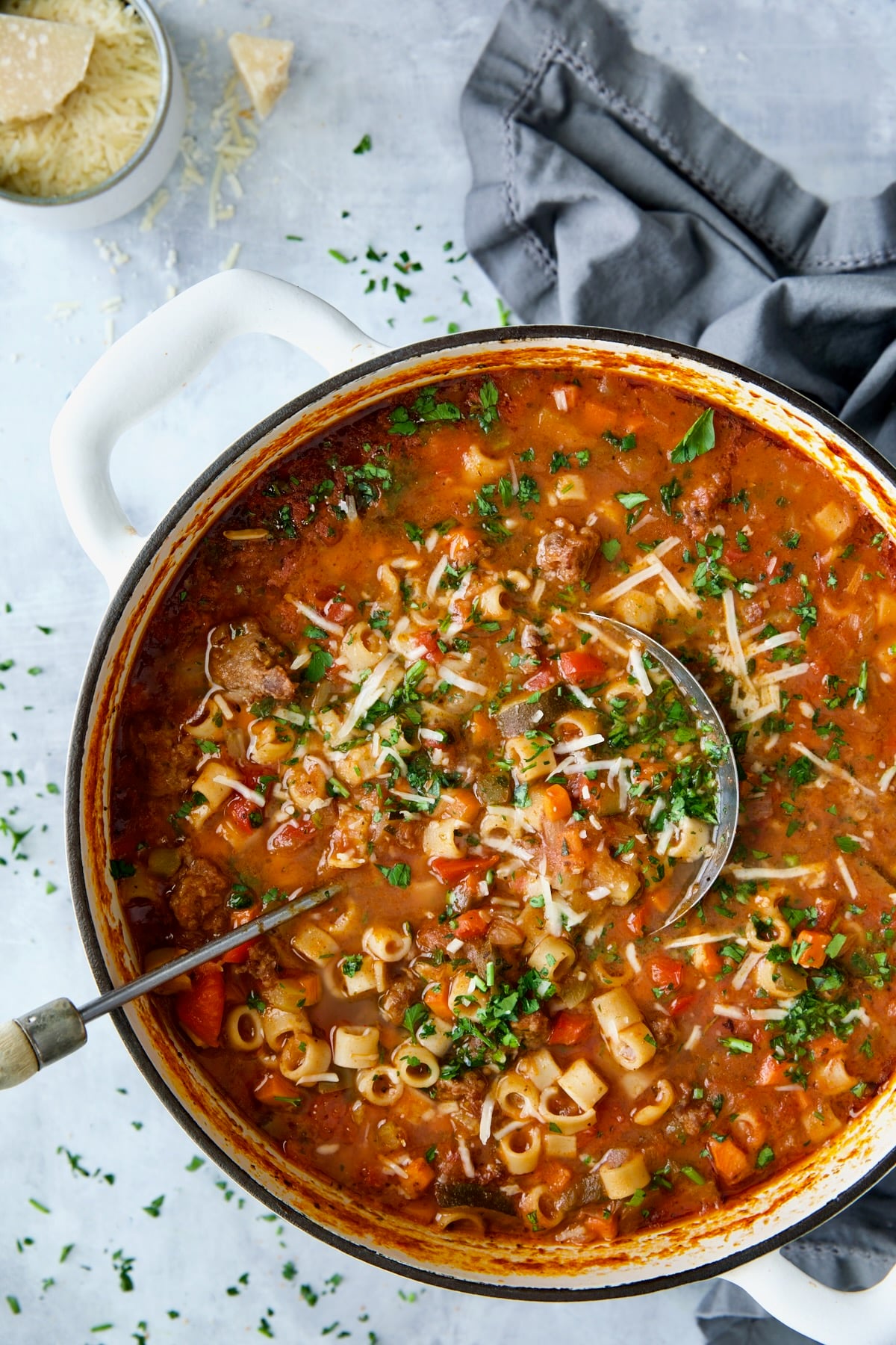 Italian Sausage Soup in white Dutch oven garnished with fresh parsley and Parmesan cheese.