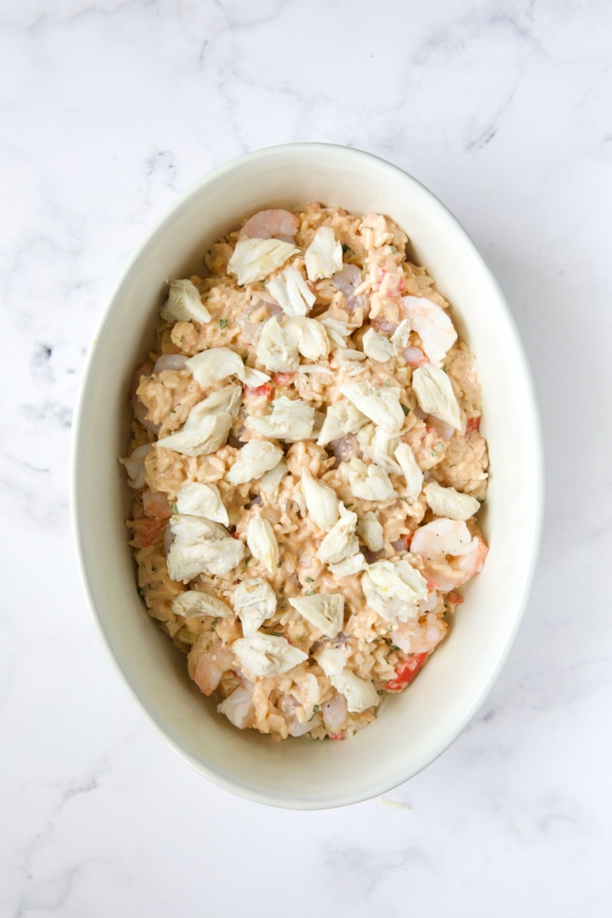 Layer of shrimp and crab over rice layer in white oval baking dish.